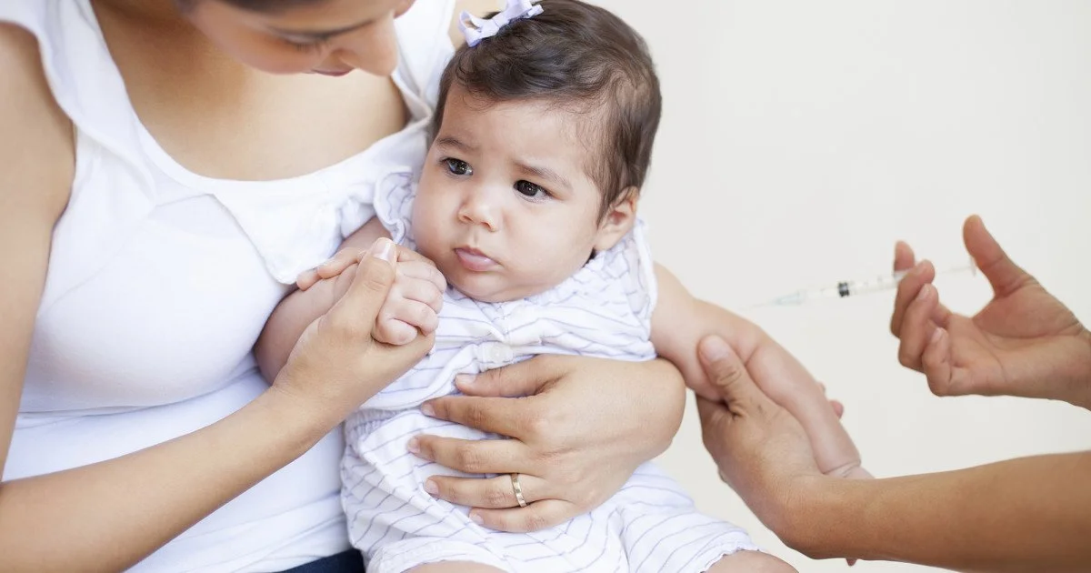 A woman holding a young girl getting vaccinated with a syringe from a healthcare worker.