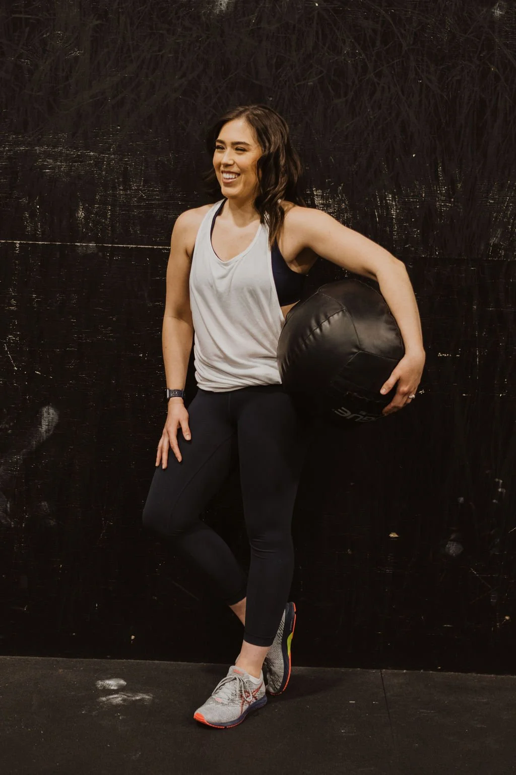 A woman Military Spouse Personal Trainer in sportswear holding a medicine ball smiling in a gym.