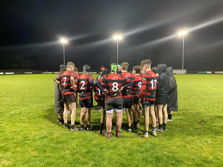 Clane RFC youth players in a huddle under floodlights