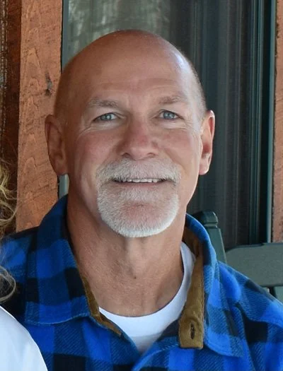 Middle-aged man with a goatee wearing a blue plaid shirt, smiling, indoors.
