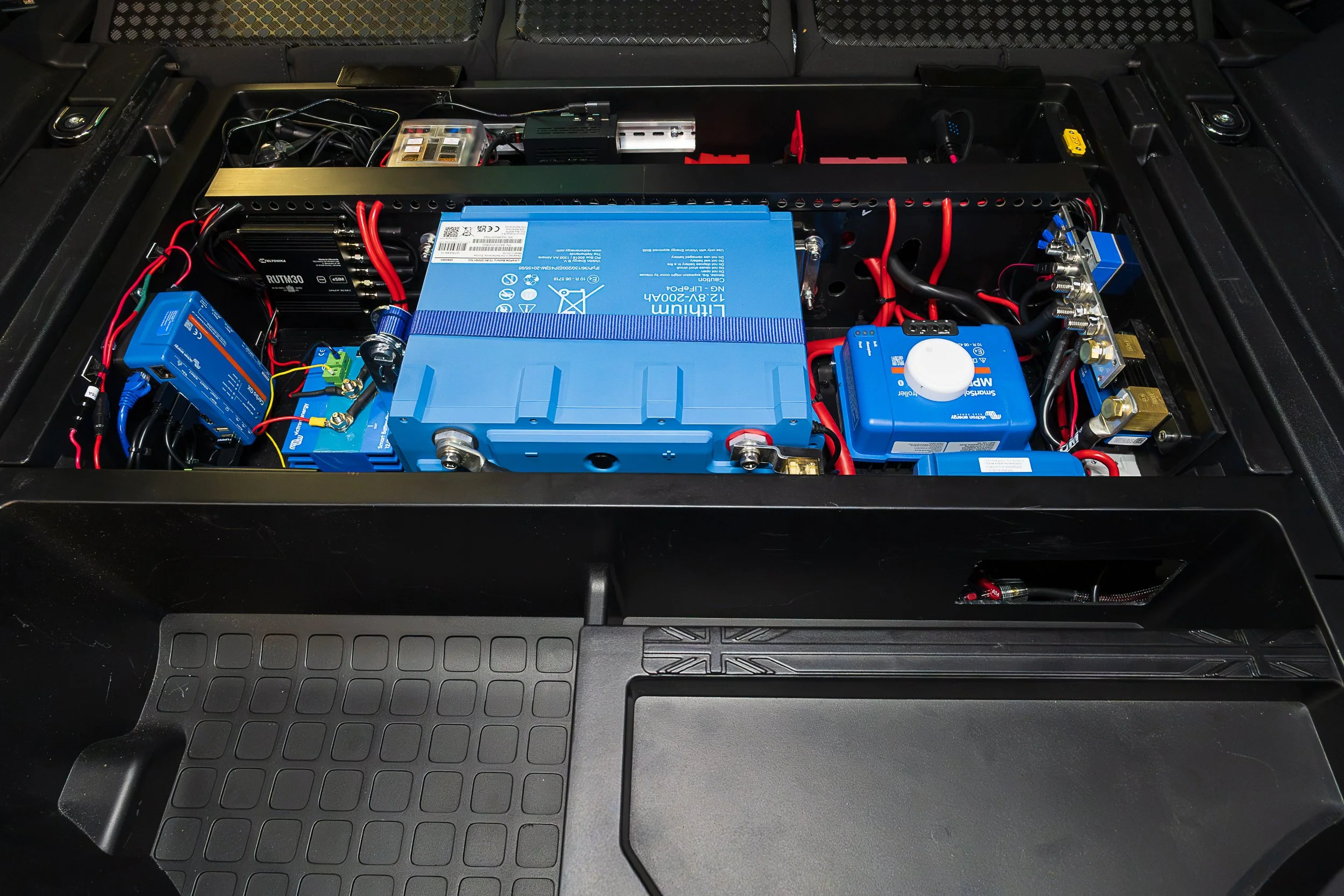 The full second-battery system tucked under the boot floor of the Defender 110. Lithium at the centre, charging and monitoring on either side.