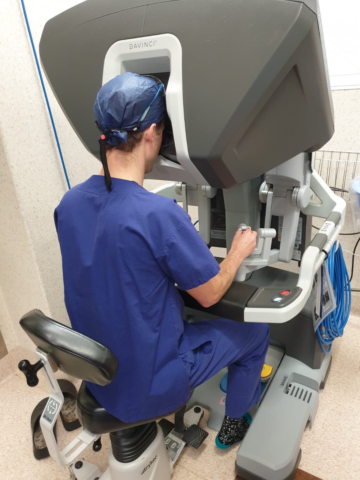 A medical professional in blue scrubs and surgical cap operating a large eye examination machine.