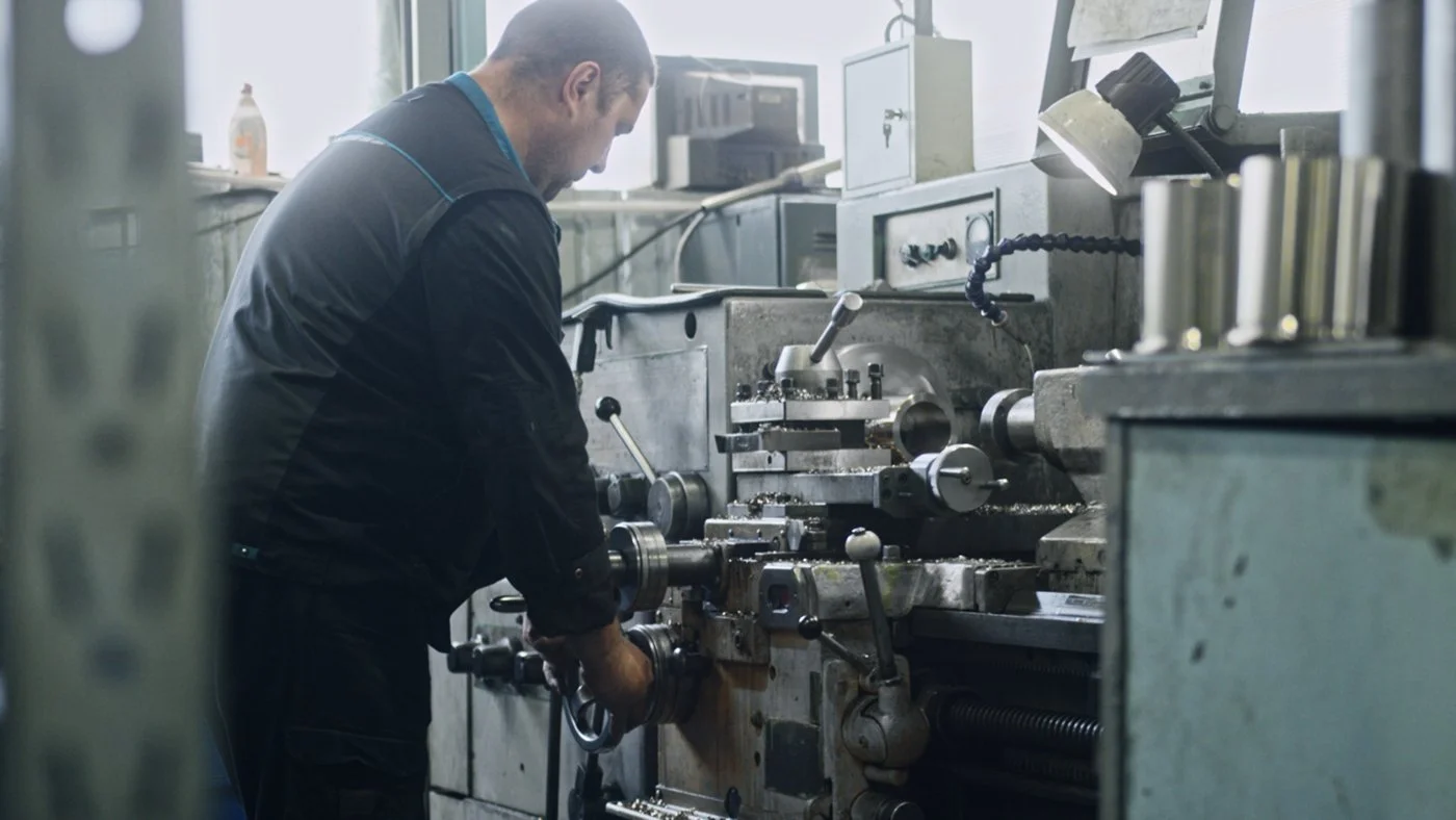 A man working on a lathe machine in a workshop or factory.