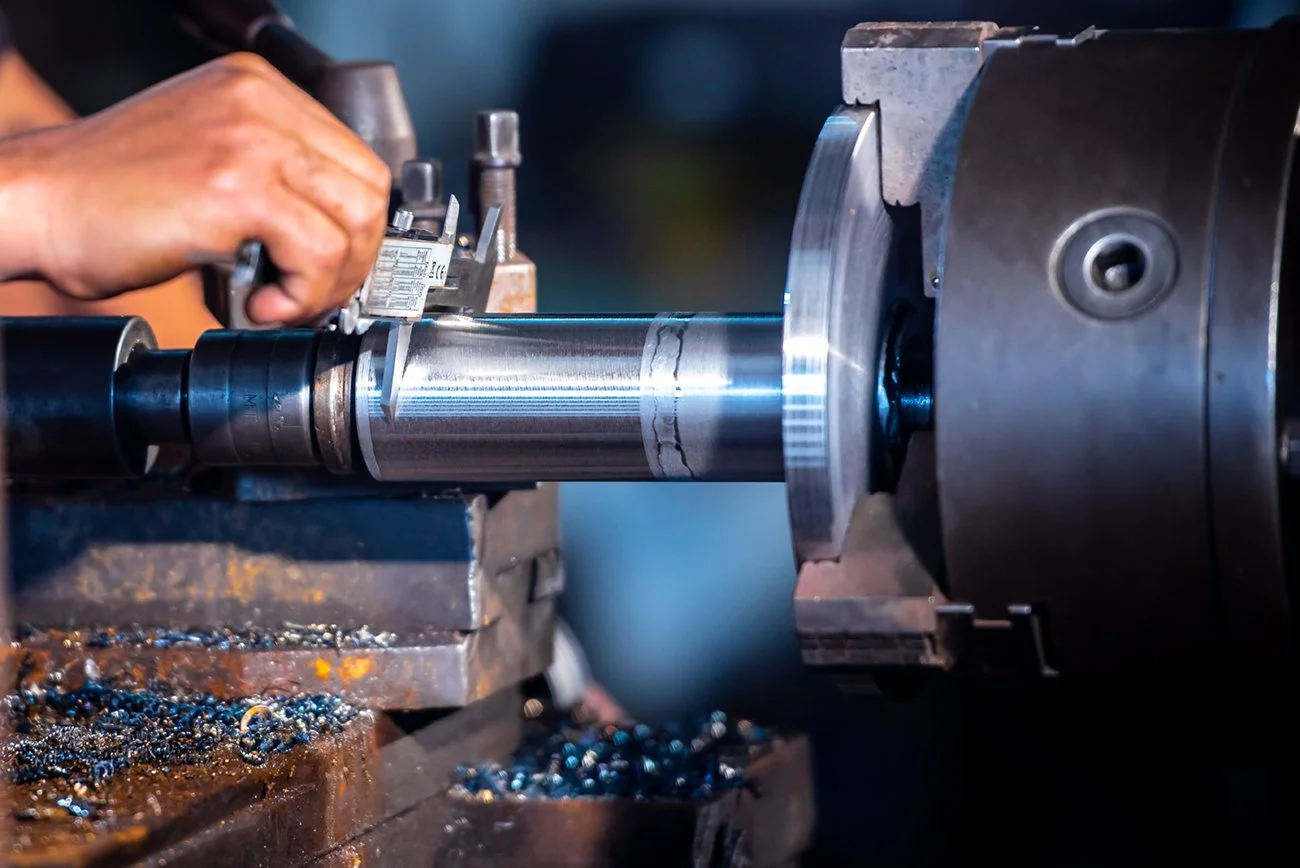 Someone's hands operating a lathe machine turning a metal shaft.