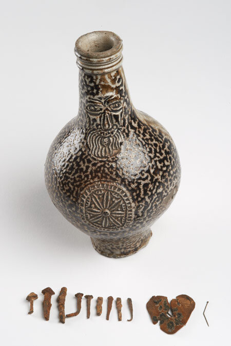  17th century stoneware Bartmann jug used as a witch bottle. Found containing a heart-shaped piece of felt pierced with pins, and eleven nails. 