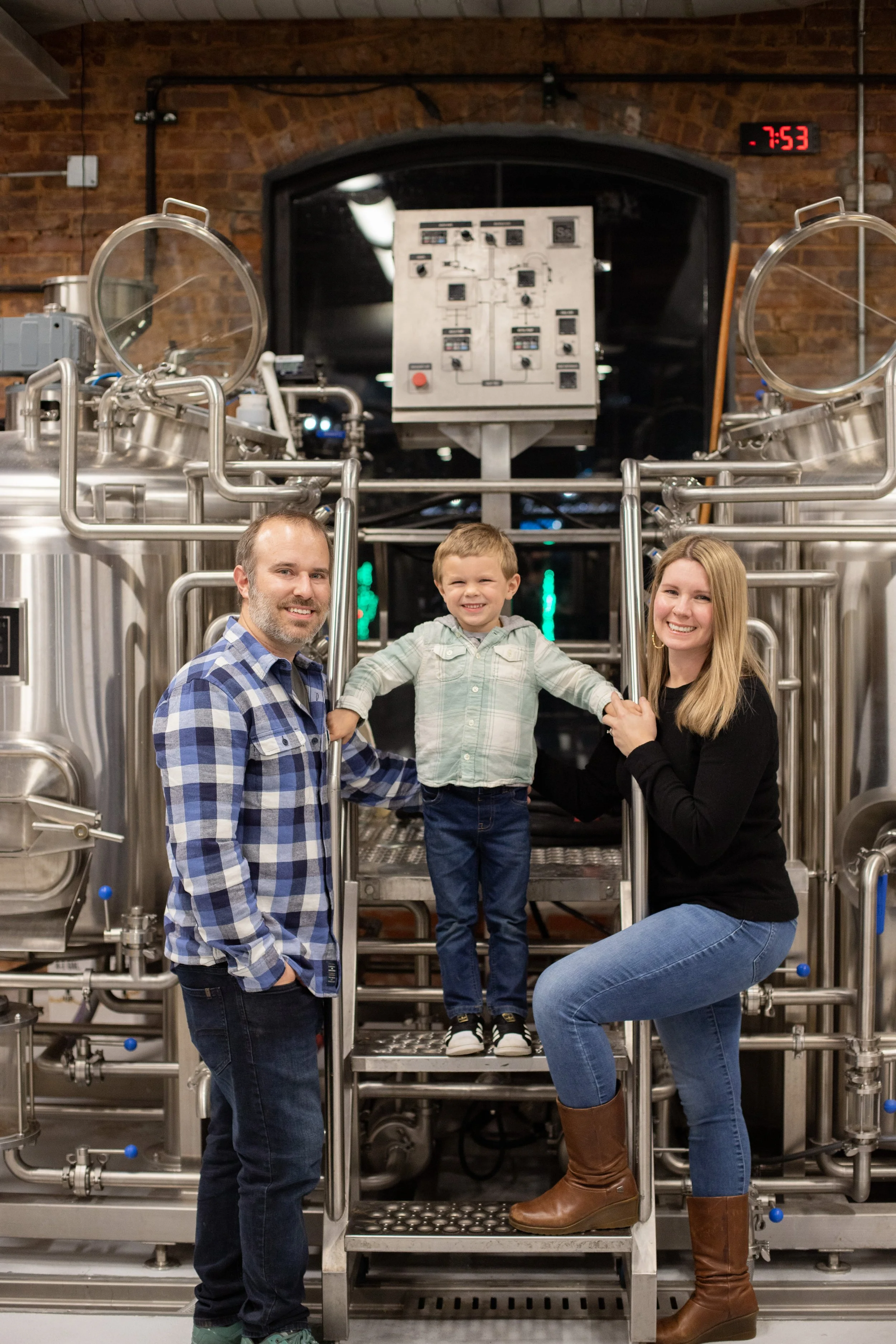 Photo of Owner Alex, his young son Liam, and wife Allison in front of the brewing system