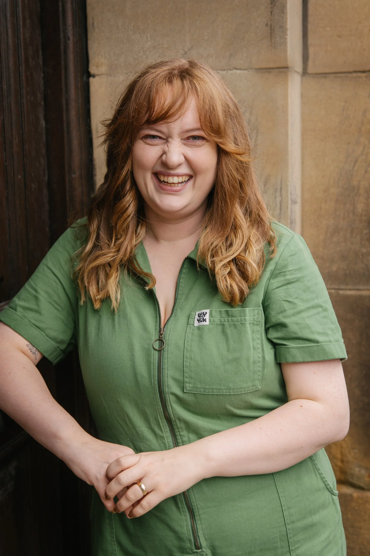 Dr Alice Ashcroft, a white woman in her thirties with red hair, leaning against a wall and smiling.