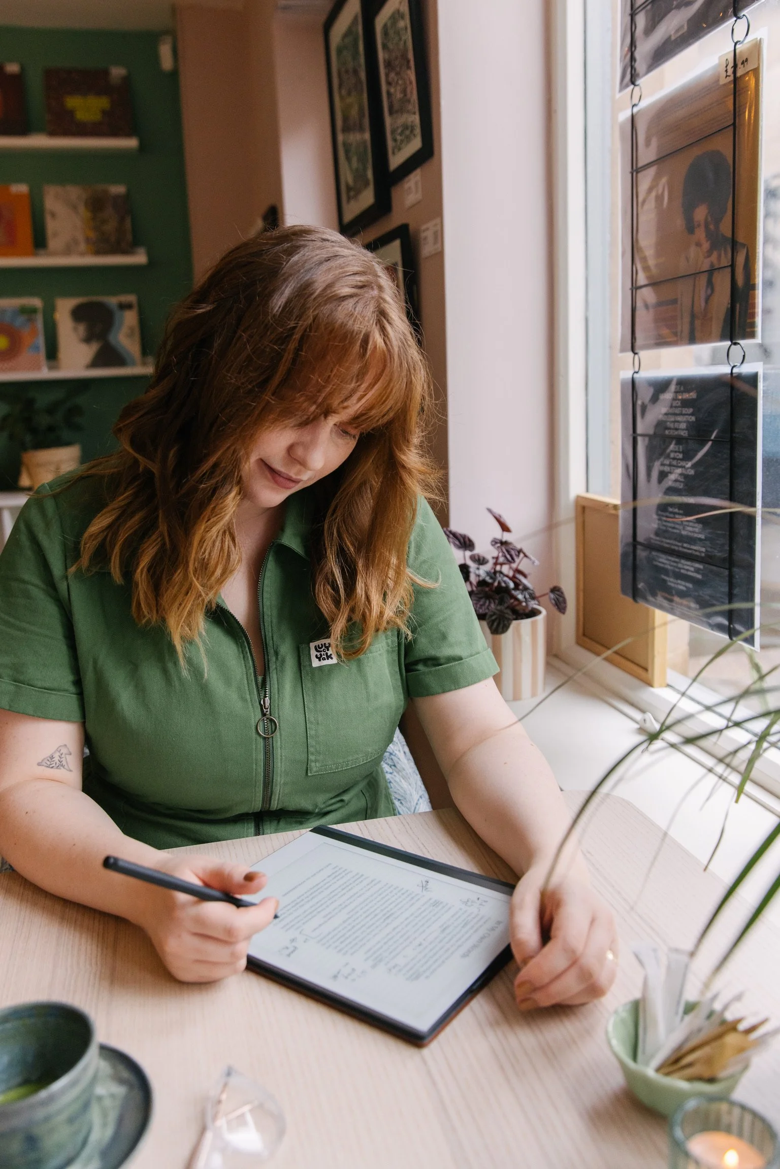 Dr Alice Ashcroft, a white woman with tattoos and red hair is looking down at her writing on a table.