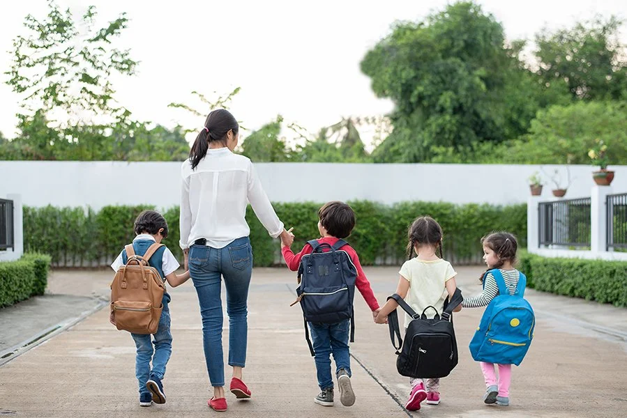 Mother and kids walking to school, kids wearing backpacks