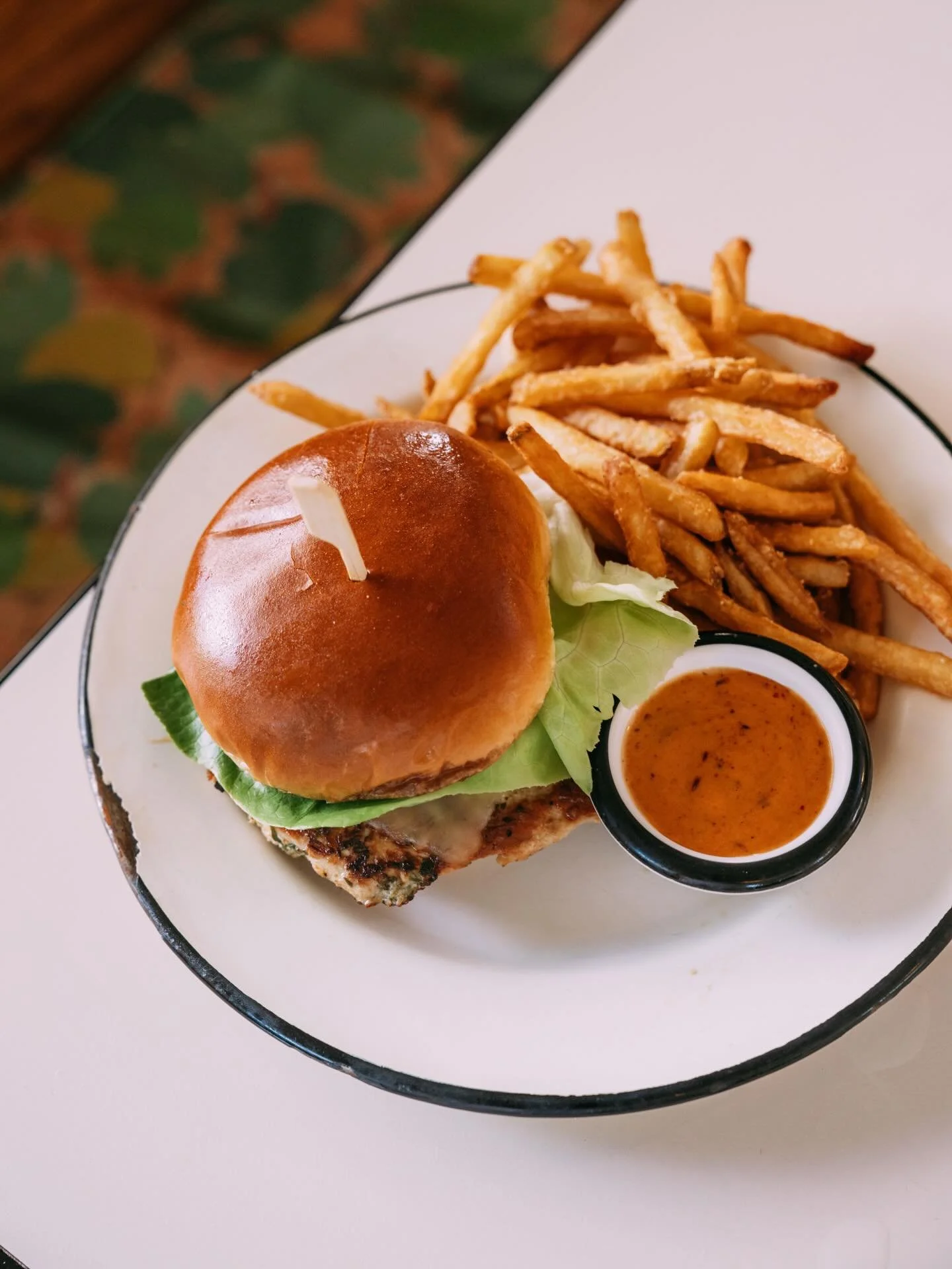 A marinated grilled chicken sandwich layered with jack cheese, lettuce, tomato, and avocado crema, finished with a honey chipotle sauce on a brioche bun, served with a side of fries 🌴🥑🍍