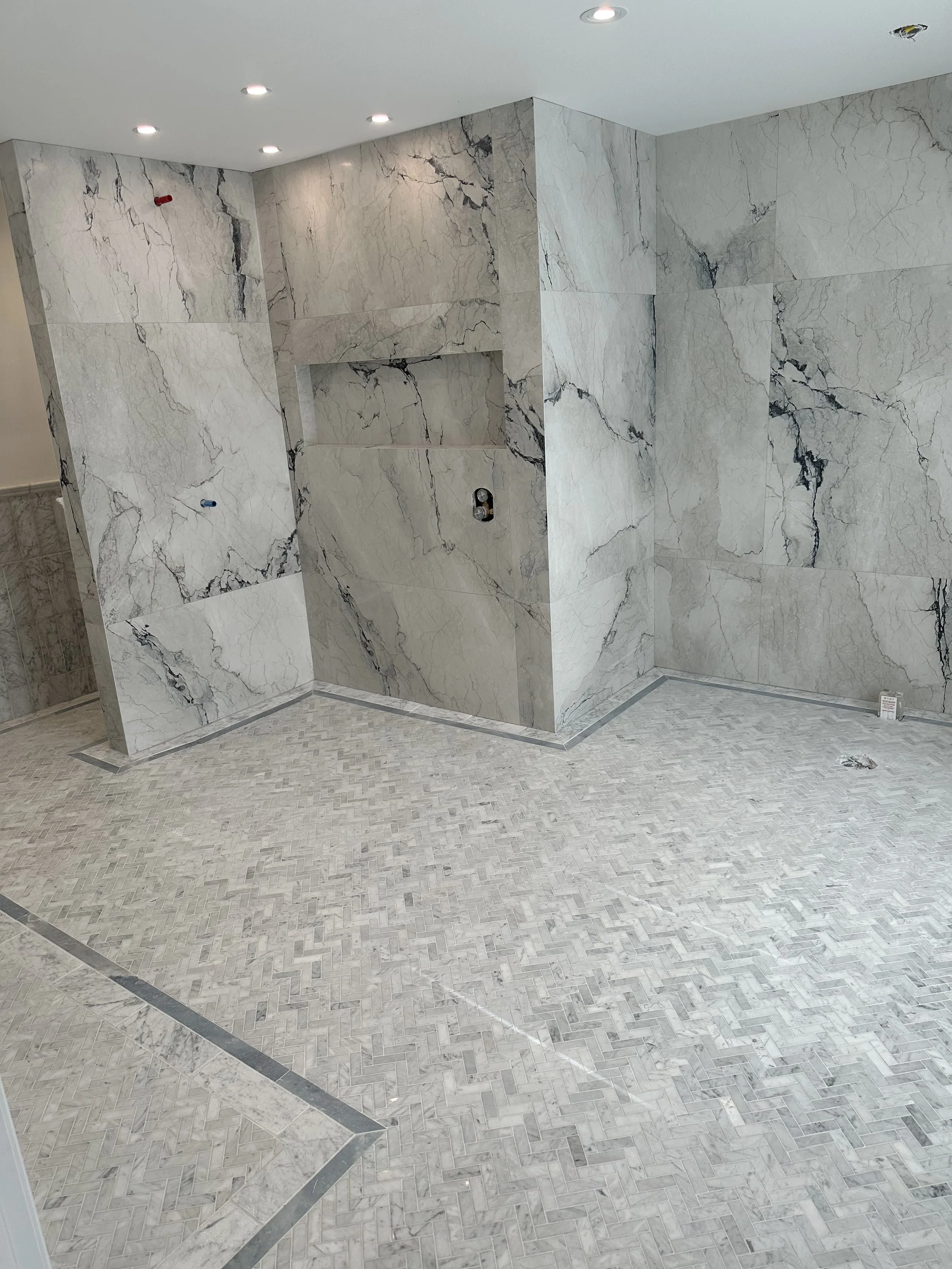 Interior of a room under construction with marble walls and tiled floor, with recessed lighting and some wiring fixtures.