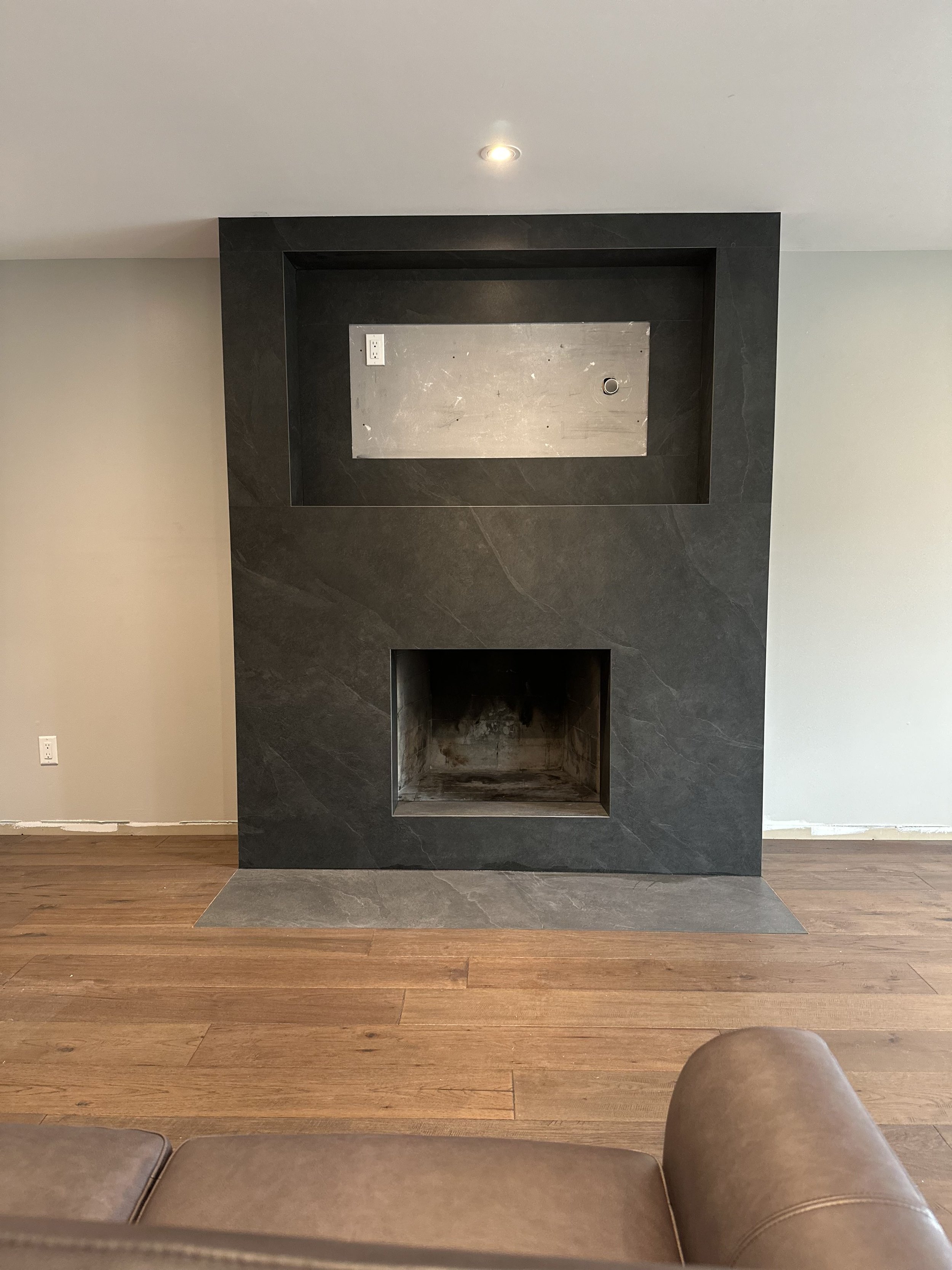 Empty fireplace with a black stone surround, metal back panel, and wood flooring.