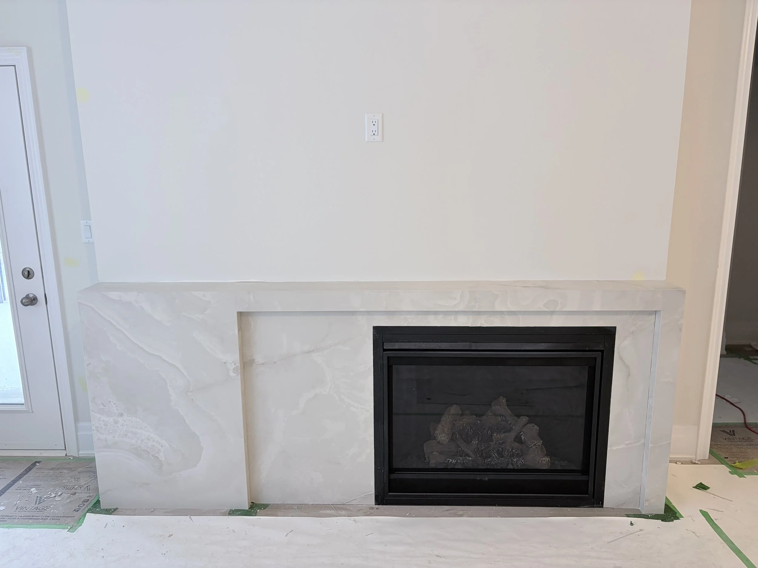 Living room fireplace with a marble surround, under construction, with protective floor coverings and an unlit firebox.