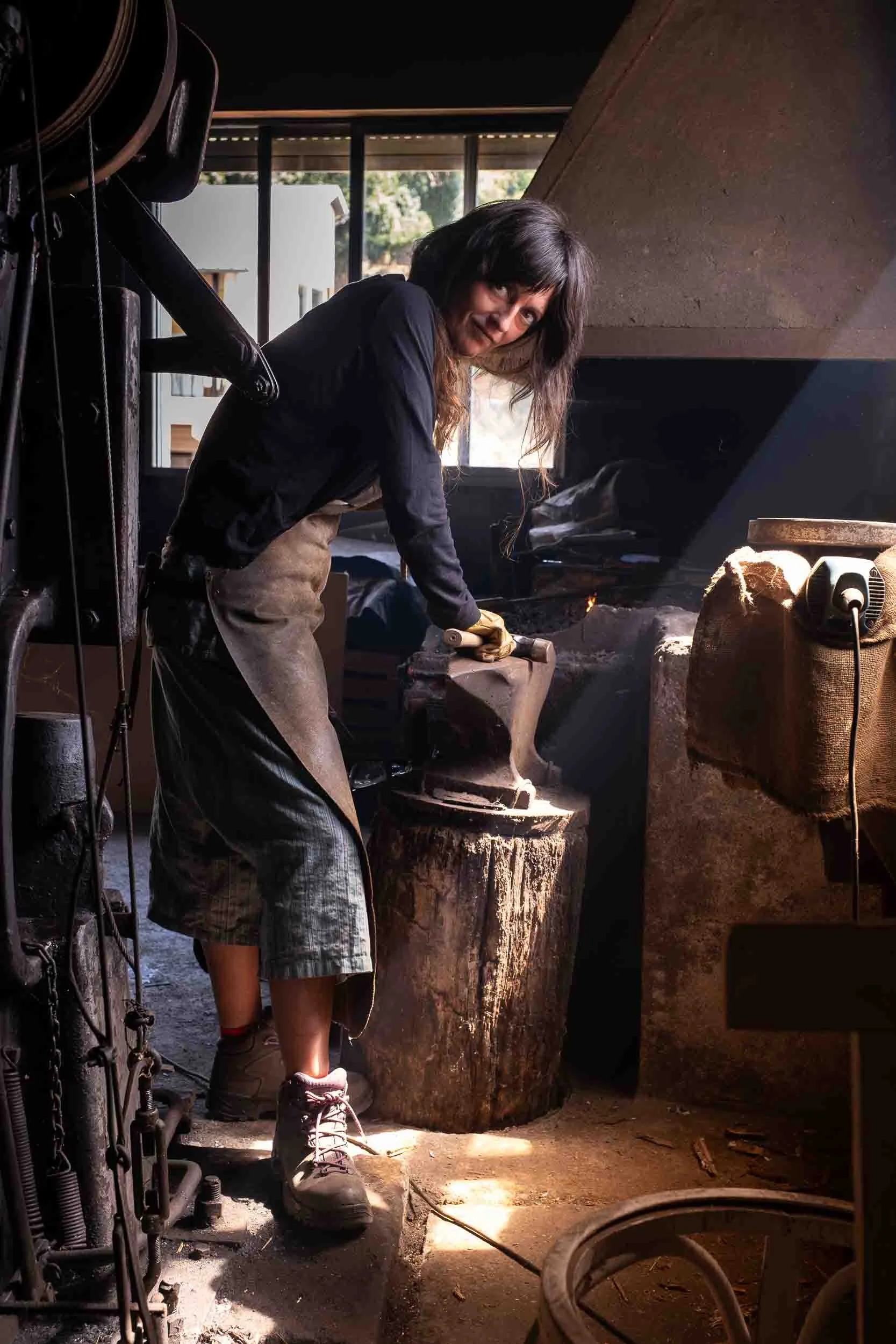 Retrato ambiental de Fátima, la artesana de Arenaysal en su taller de forja. La iluminación dramática resalta la concentración y el entorno rústico y ancestral.