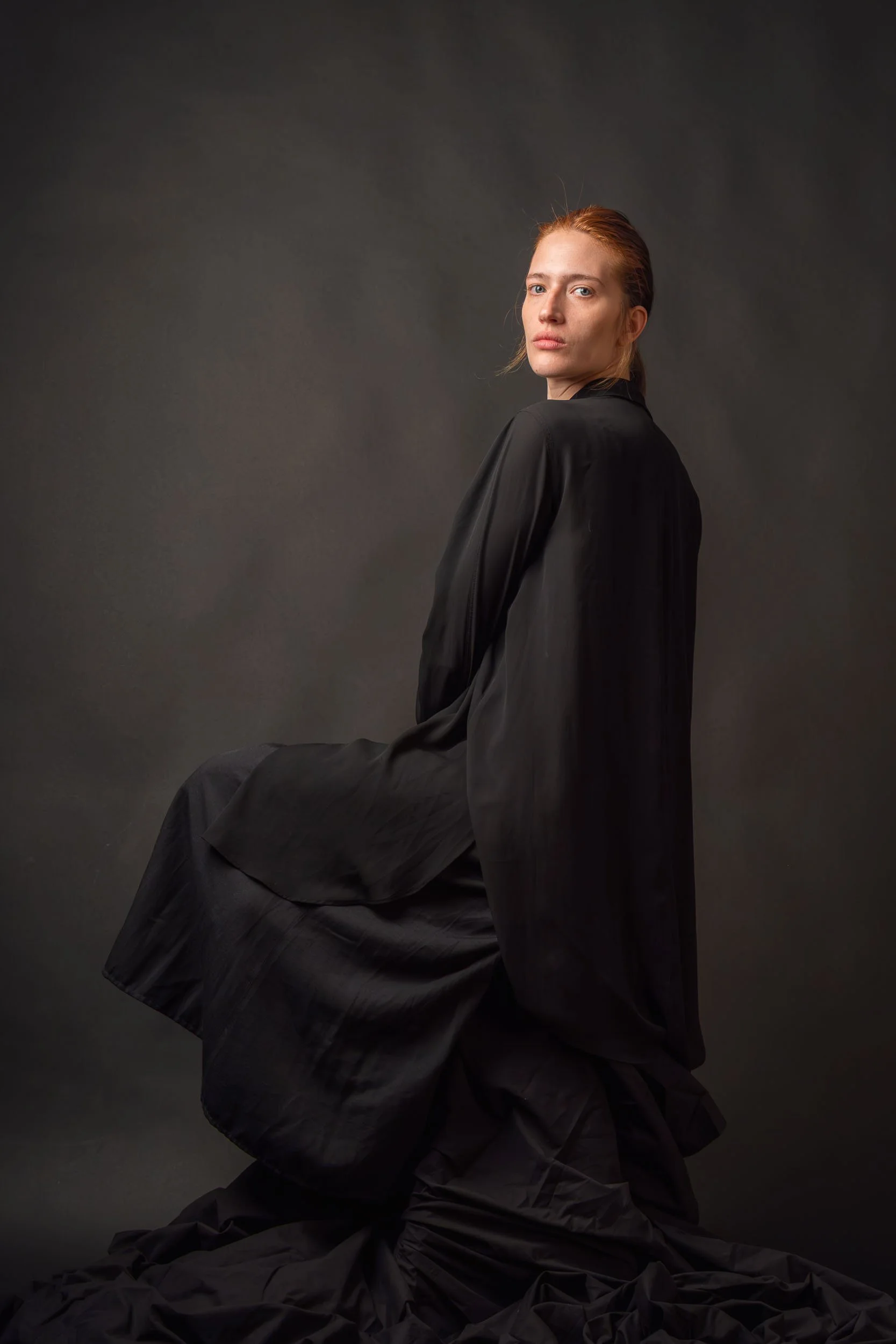 Retrato artístico en clave baja de una modelo con vestido oscuro, resaltando sombras y una atmósfera de misterio y elegancia.