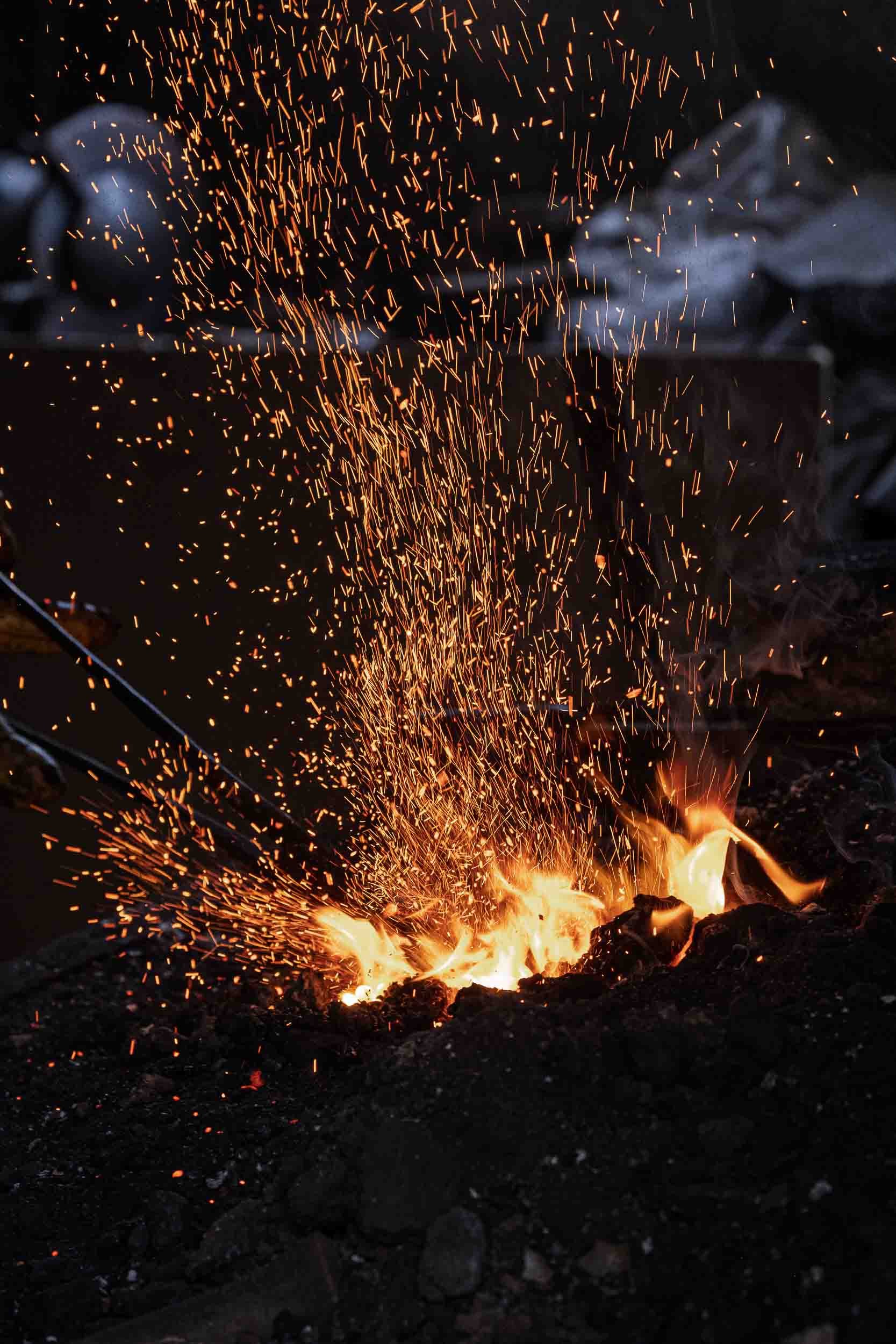 Detalle artístico de chispas saltando desde el fuego de la fragua durante el proceso de forjado