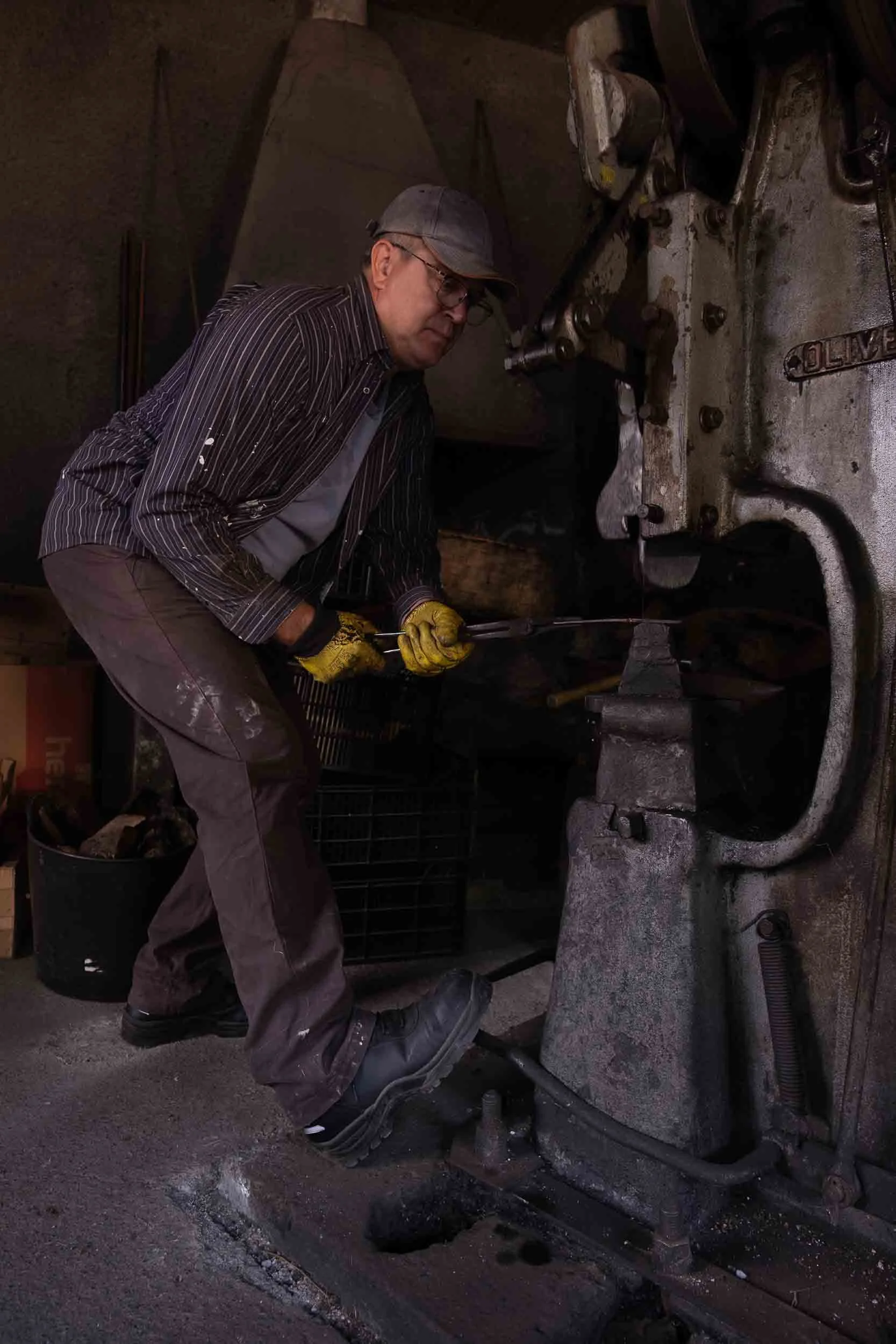 Herrero artesano forjando la hoja de un cuchillo con mazo sobre el yunque, chispas y metal incandescente en la fragua.