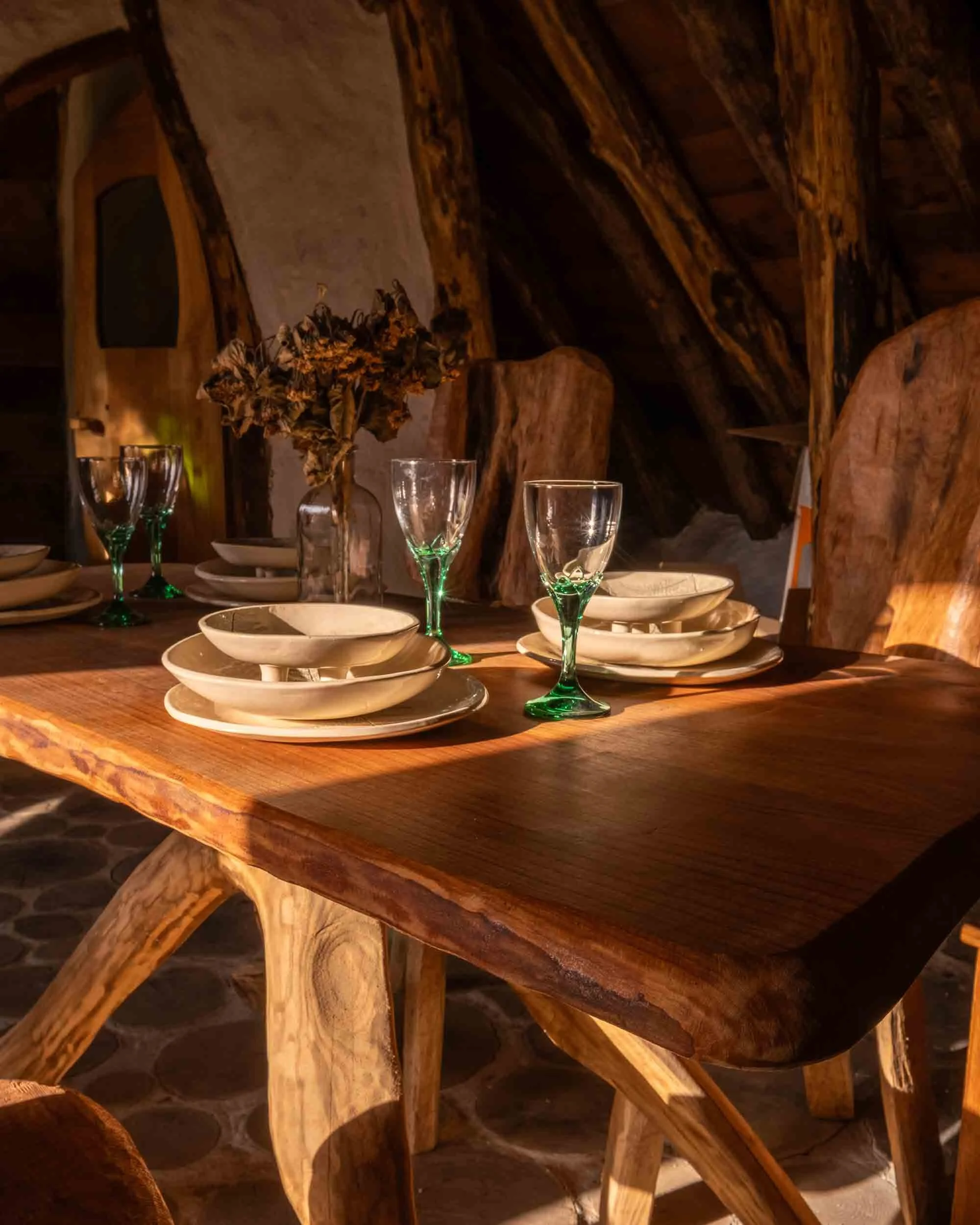 Interior de cabaña de diseño rústico inspirado en casas hobbit, con paredes curvas de piedra y mobiliario de madera artesanal bajo luz cálida.