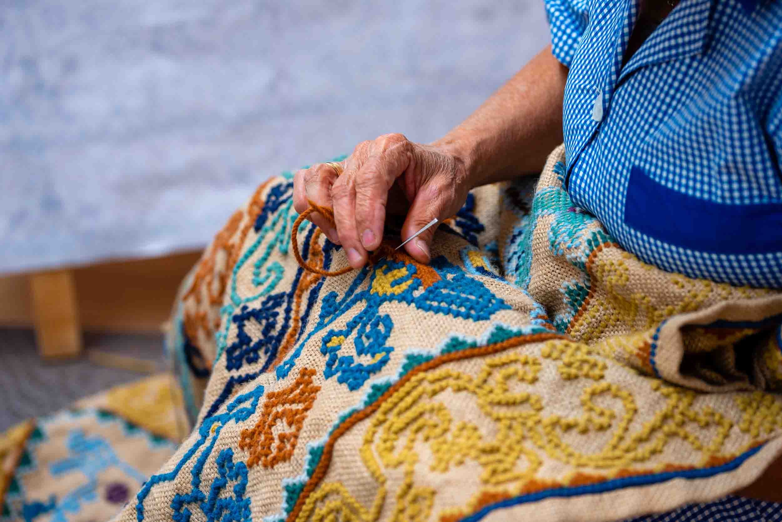 Costurera trabajando minuciosamente en la creación de un tapiz artesanal, fotografía de paciencia y detalle textil.