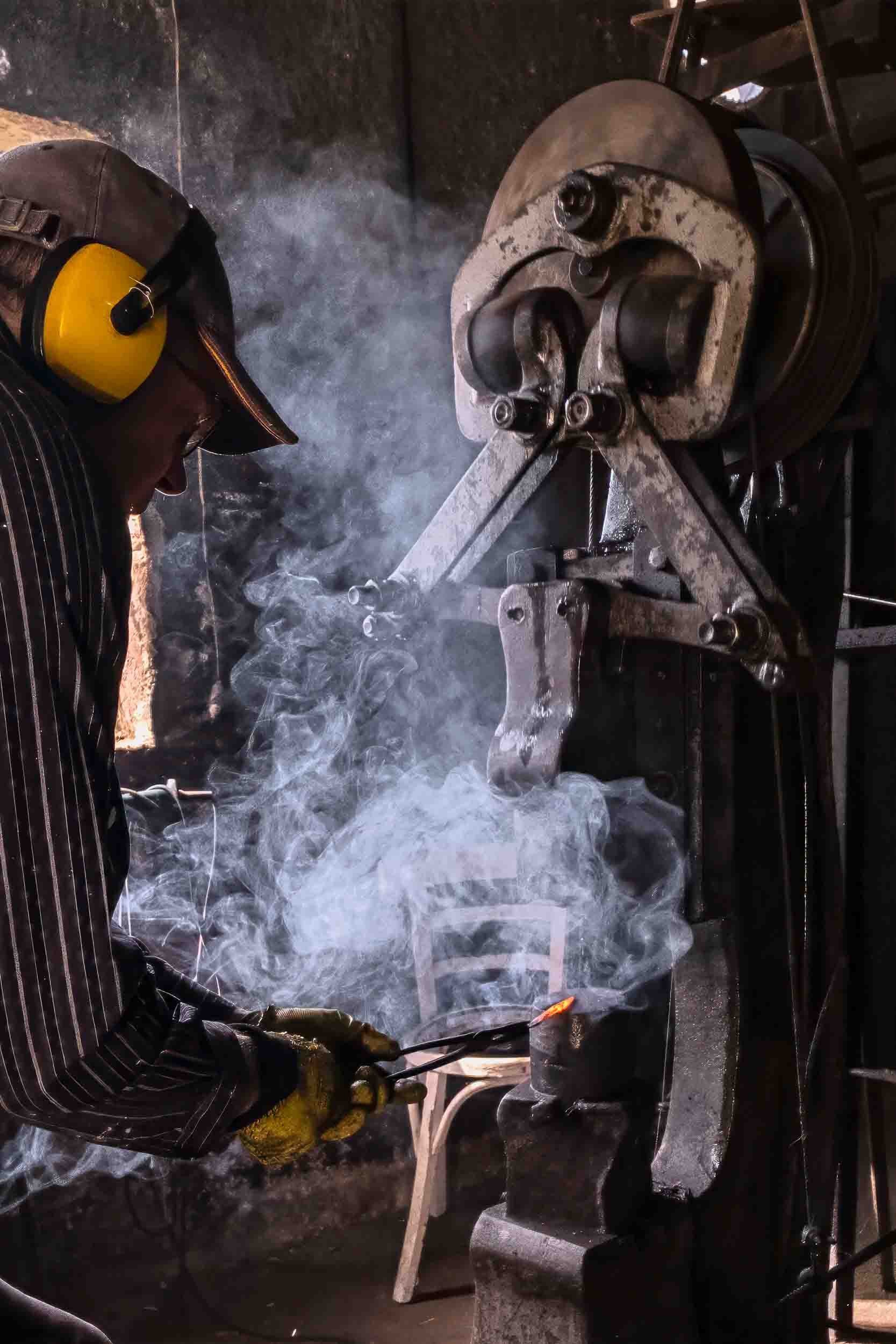 Primer plano de un mazo golpeando metal incandescente entre nubes de humo en la forja de Riotorto.
