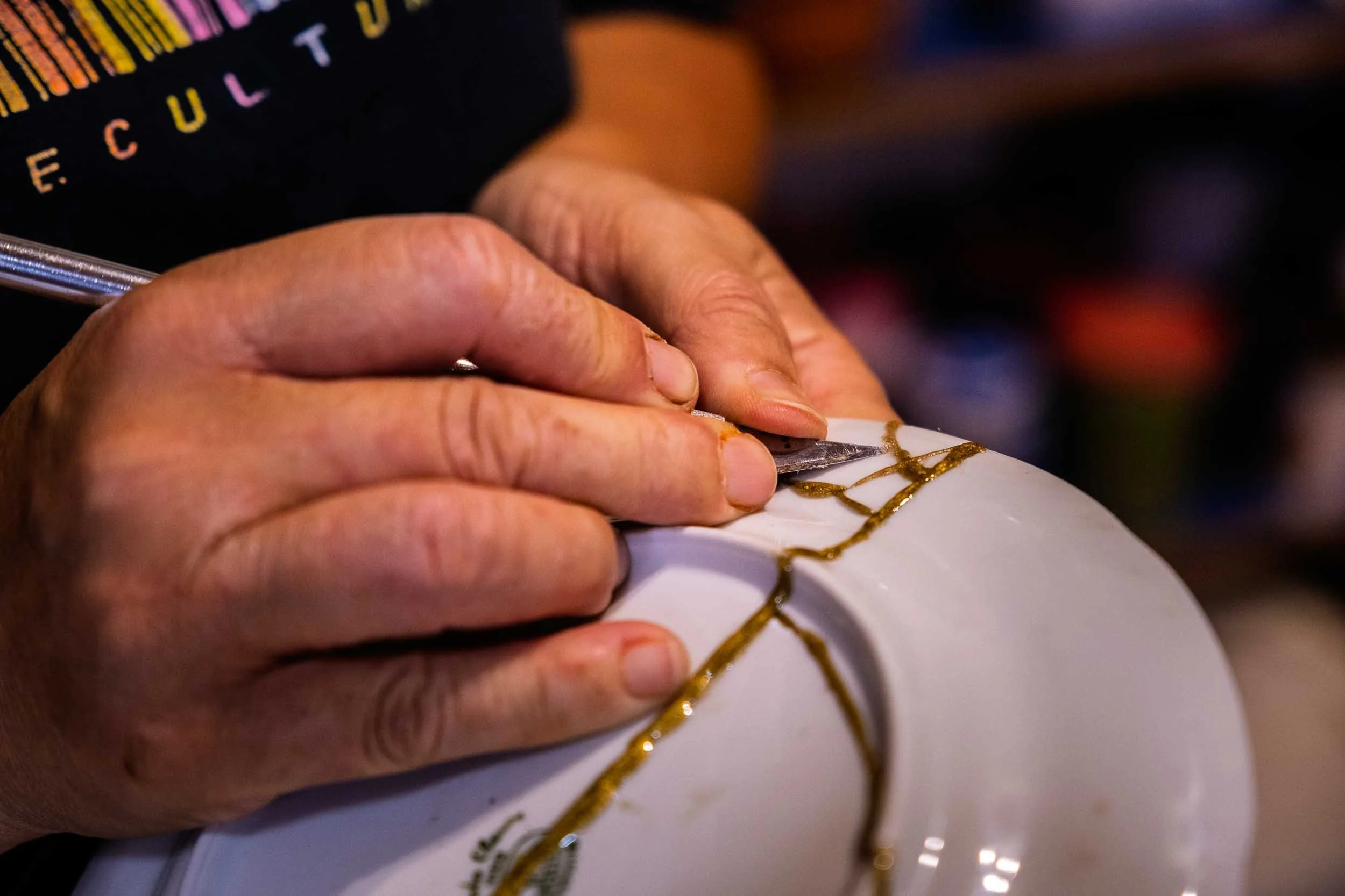 Primer plano de manos aplicando con precisión la técnica japonesa de Kintsugi para unir piezas de cerámica con oro.