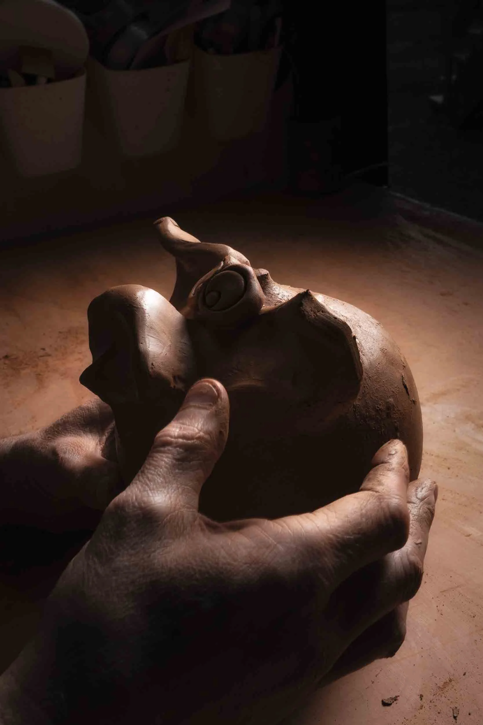 Detalle artístico a contraluz de las manos del alfarero moldeando el barro húmedo. Fotografía que captura la delicadeza y la fuerza del oficio.