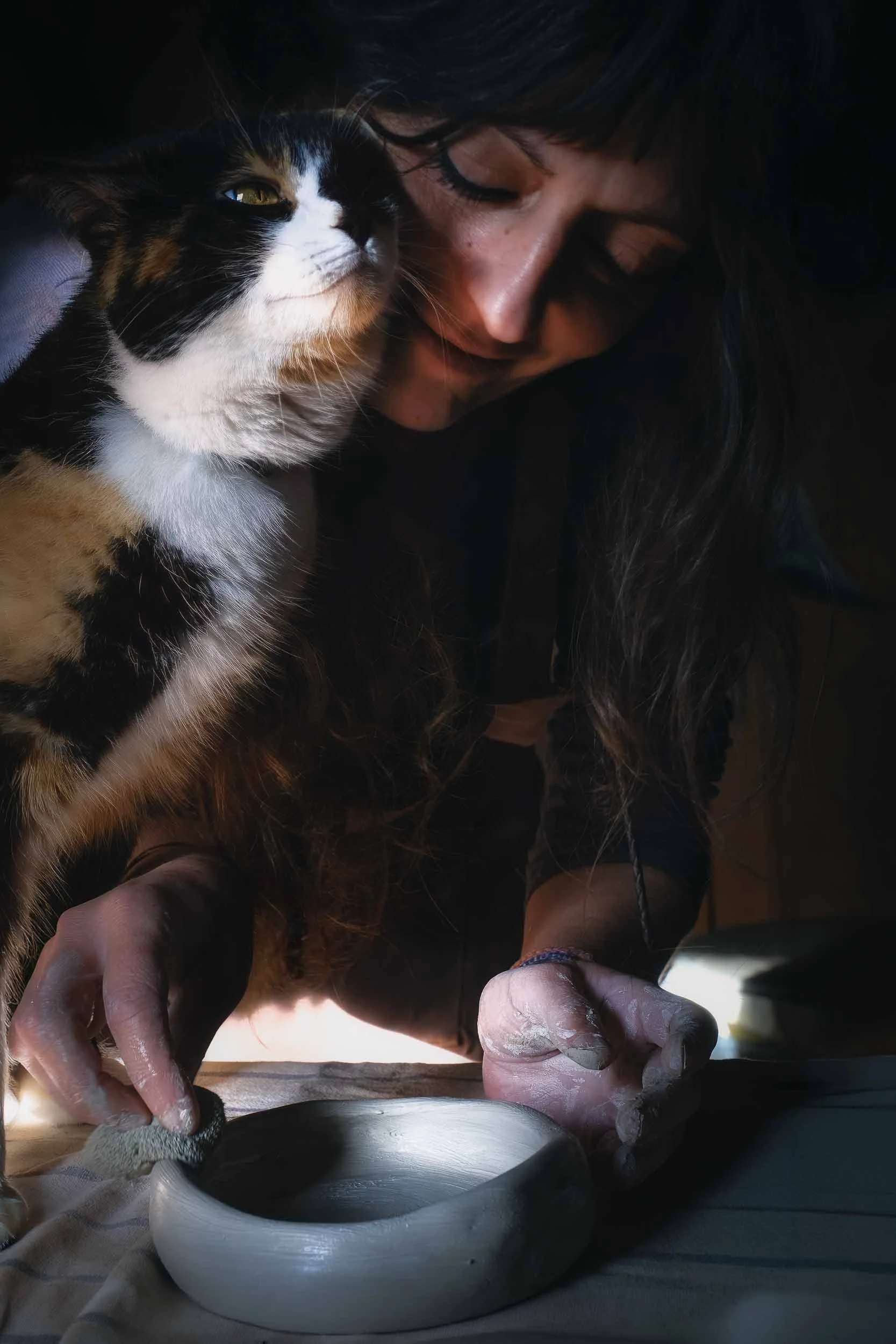 Retrato ambiental de la artesana moldeando barro en su taller rústico, acompañada por su gata y musa Lúa. Una imagen que transmite calma, autenticidad y la vida rural.