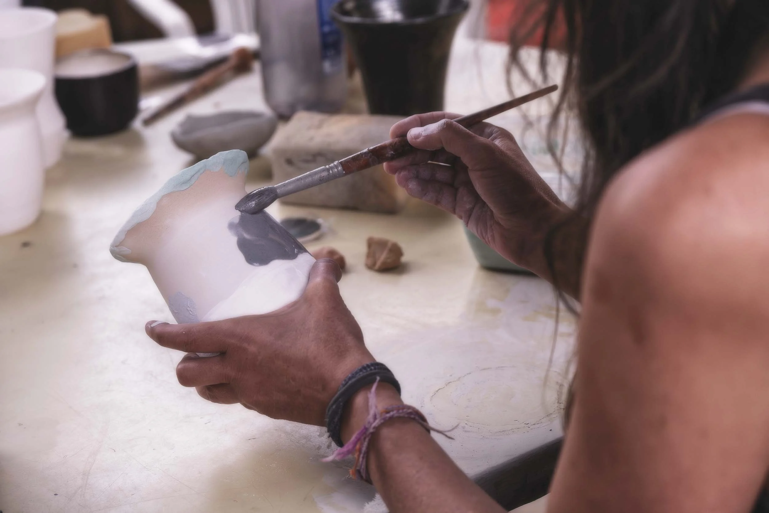 La artesana de Arena y Sal aplicando esmalte a una pieza de cerámica antes de la cocción Raku. Fotografía documental que muestra la delicadeza del proceso previo al fuego.
