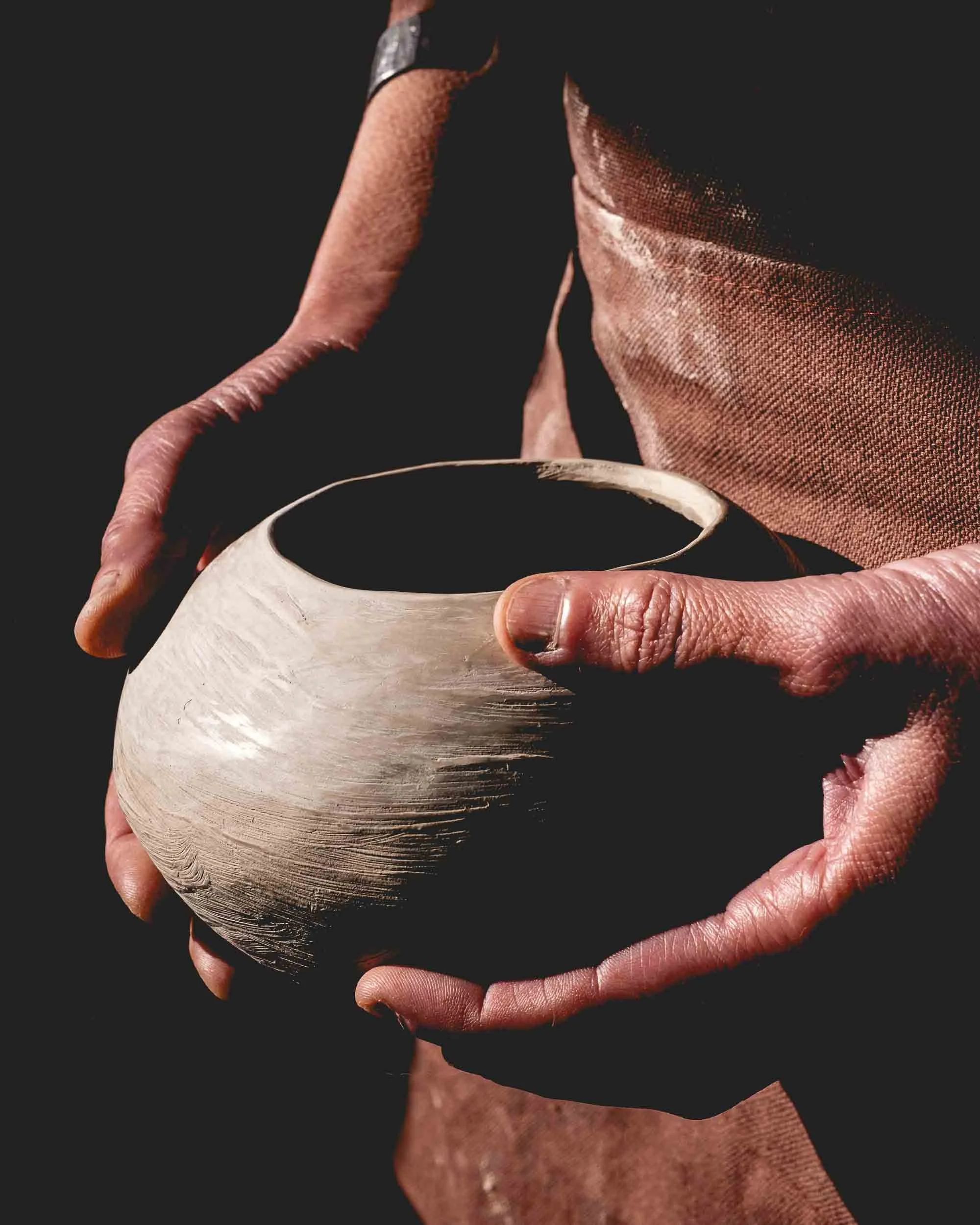 Manos de la artesana sosteniendo una vasija de barro negro recién moldeada, un ejemplo de la técnica de cocción ancestral sin oxígeno