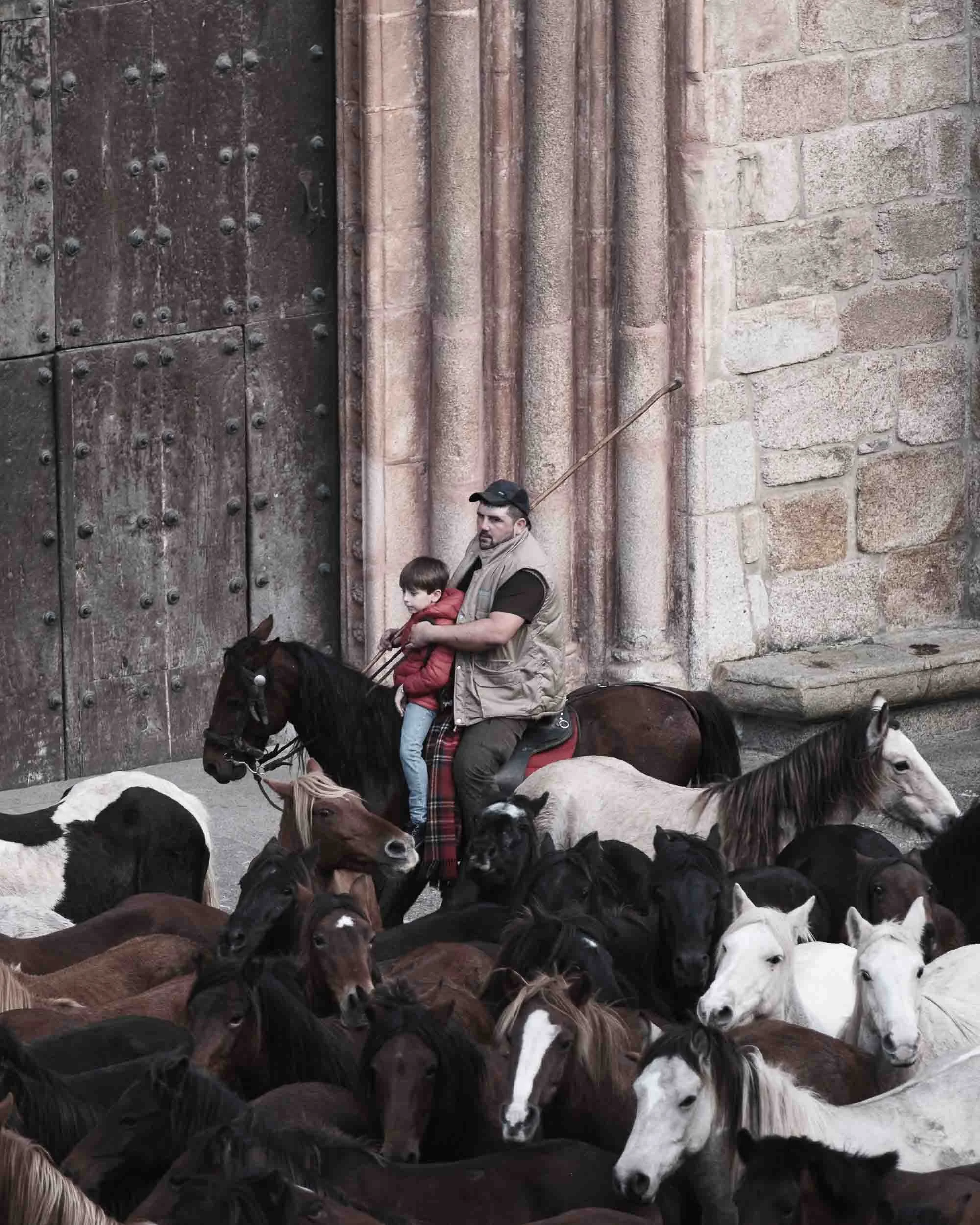 Un jinete montado a caballo llevando a su hijo, simbolizando el relevo generacional y la pasión por la feria de As San Lucas en las familias de la comarca.