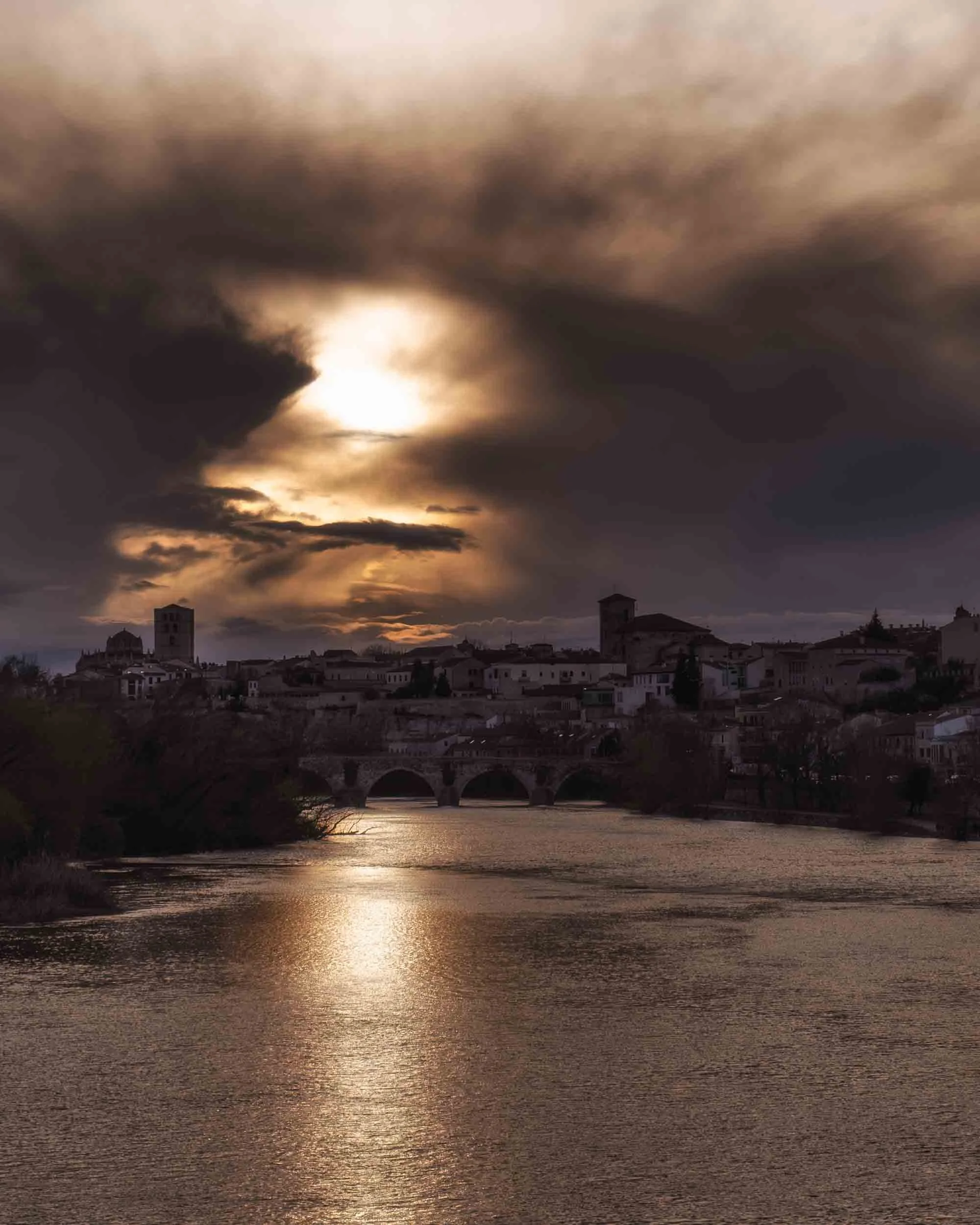 Vista de la ciudad de Zamora sobre el río Duero en un atardecer dramático, capturando su esencia monumental y la luz sobre la piedra románica.