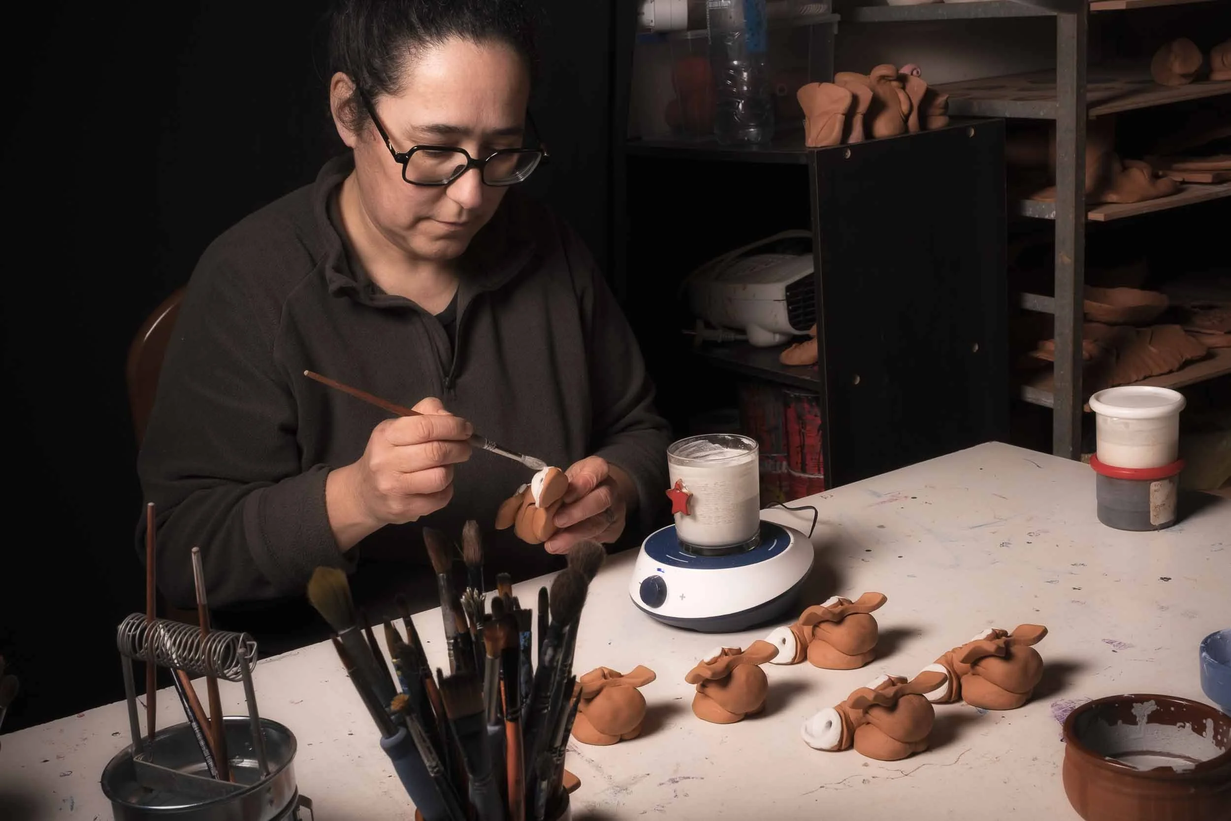 La ceramista Maica aplicando esmalte a las piezas de cerámica acabadas. Detalle del proceso de finalización y color.