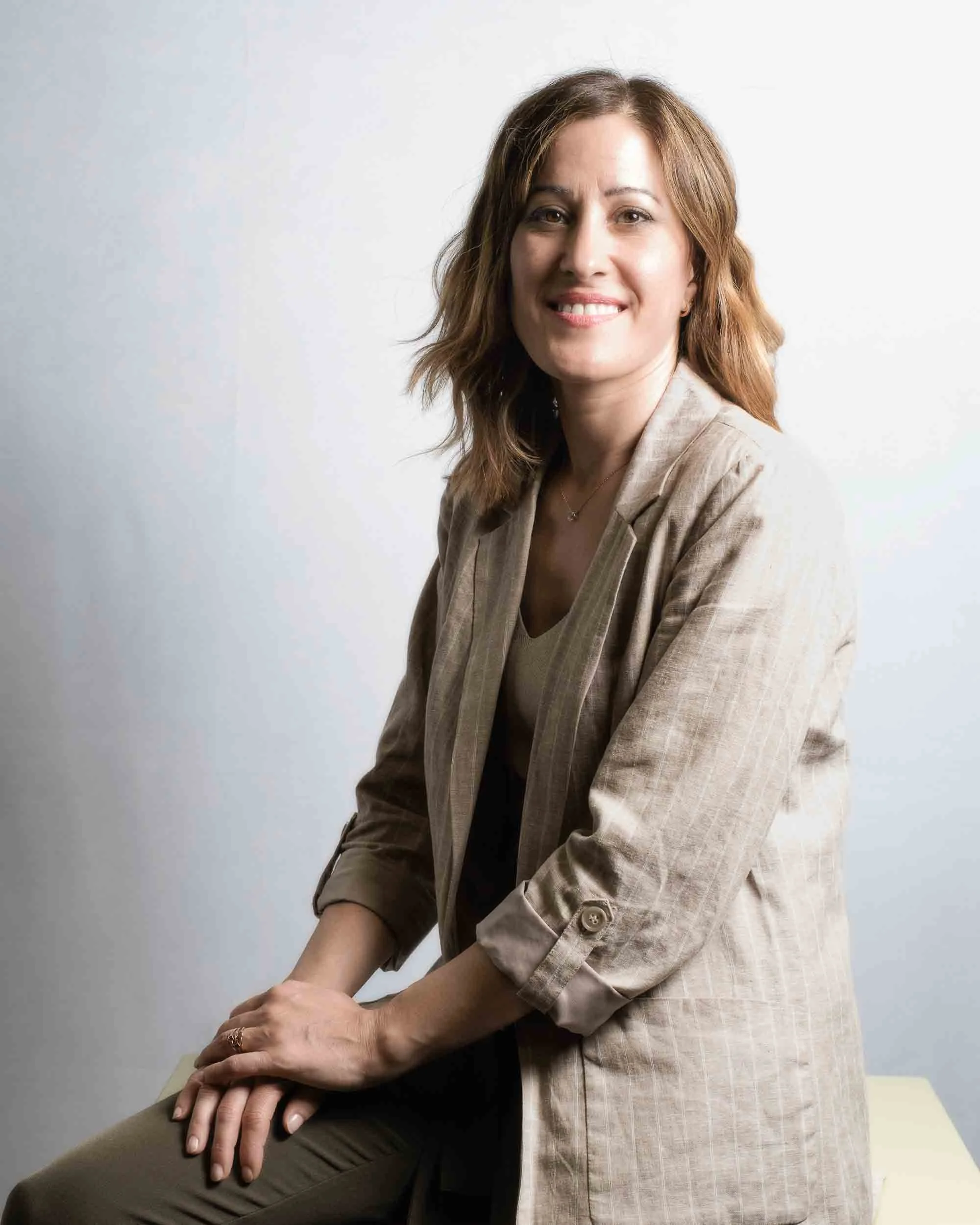 Retrato de medio cuerpo de candidata municipal. Pose lateral con mirada directa a cámara, transmitiendo una mezcla de amabilidad y firmeza ejecutiva sobre fondo gris minimalista.