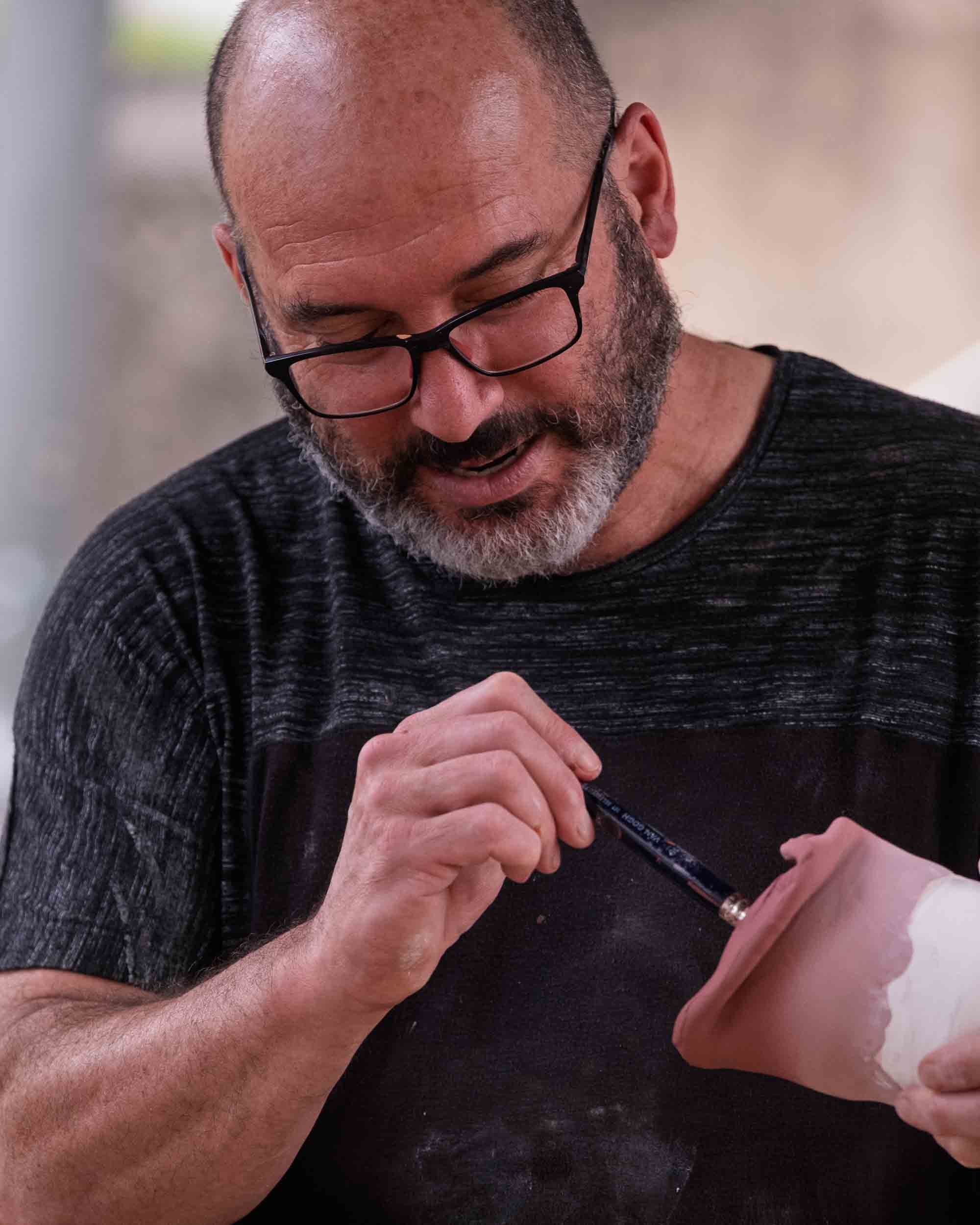 Retrato del maestro alfarero Marcelo concentrado mientras decora una pieza con un pincel fino.
