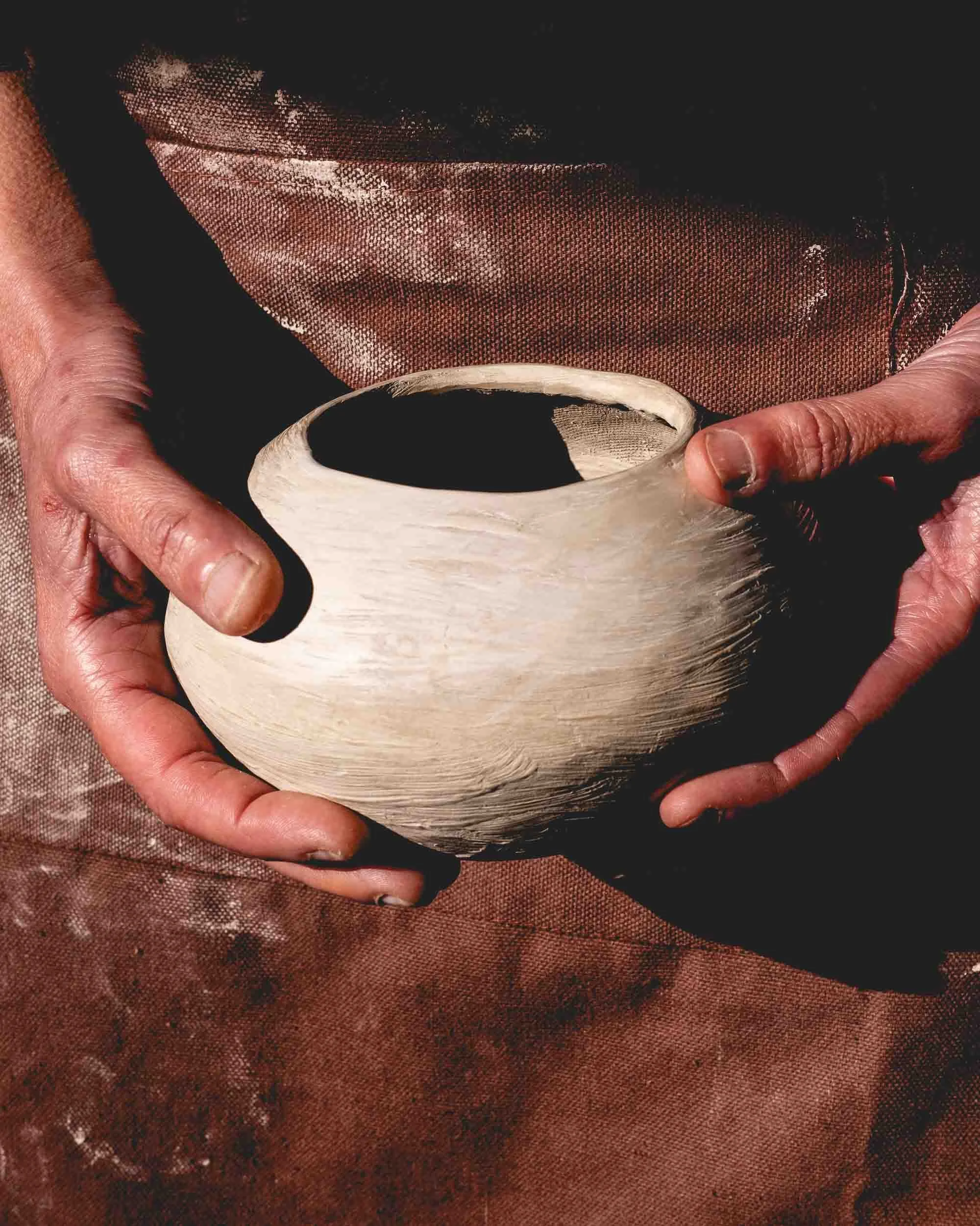 Manos de la artesana sosteniendo una vasija de barro negro recién moldeada, un ejemplo de la técnica de cocción ancestral sin oxígeno