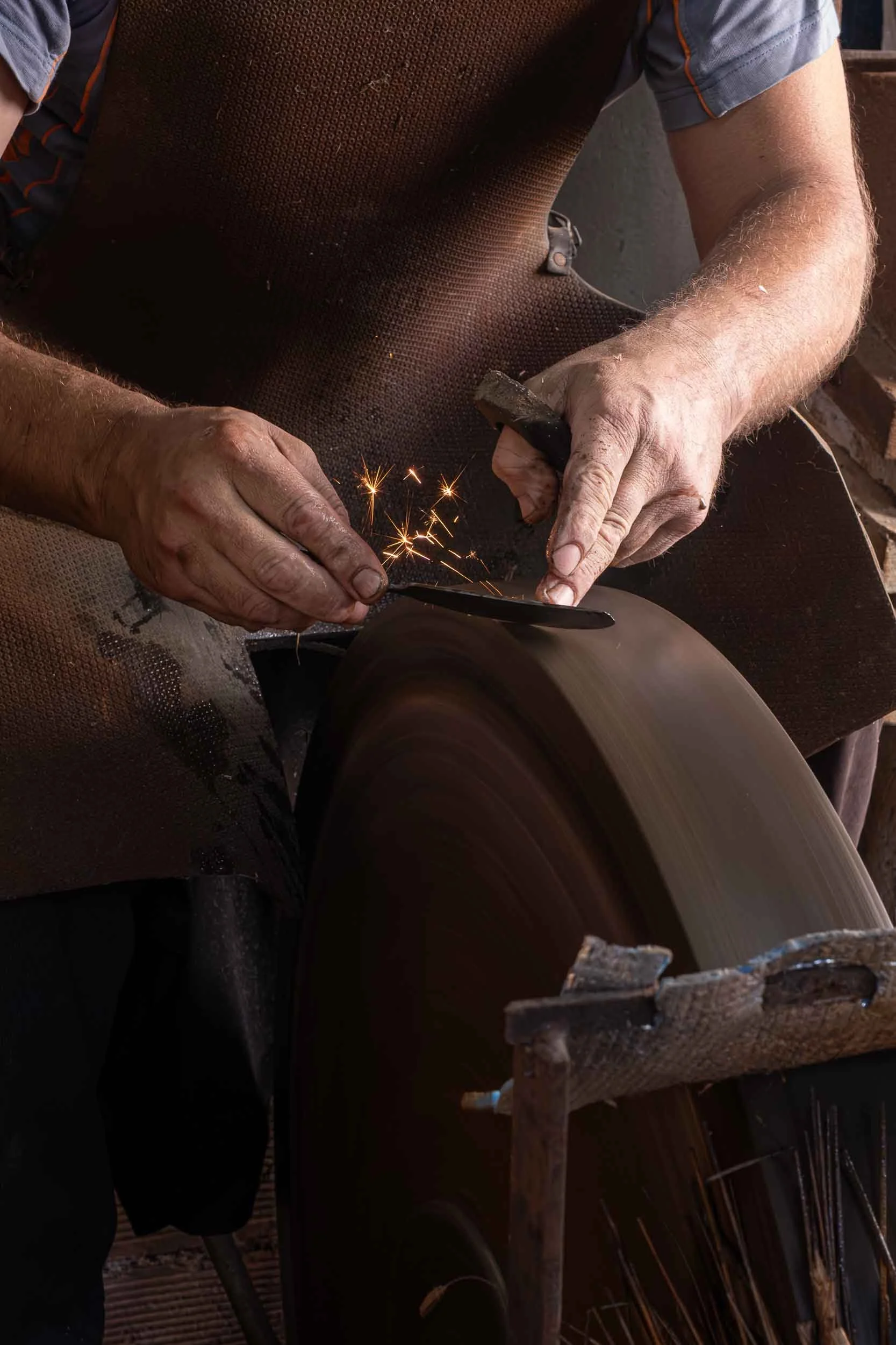 Manos de ferreiro de Riotorto dando filo a una herramienta de corte en la piedra de afilar