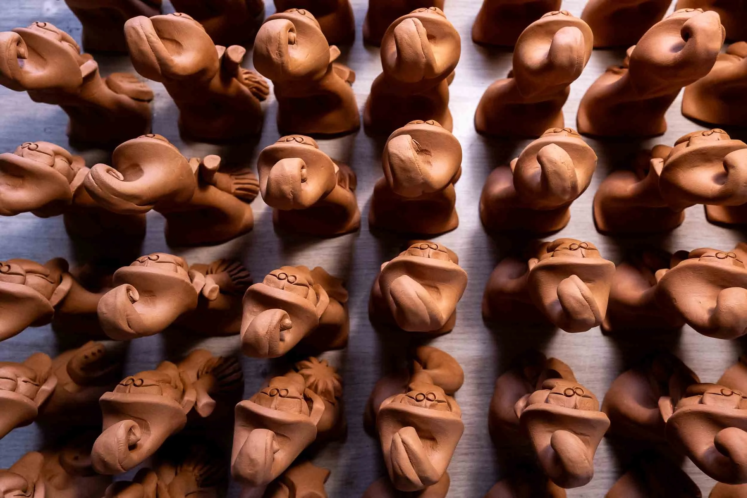 Vista cenital de decenas de pequeñas figuras de barro dispuestas en filas para el proceso de secado.