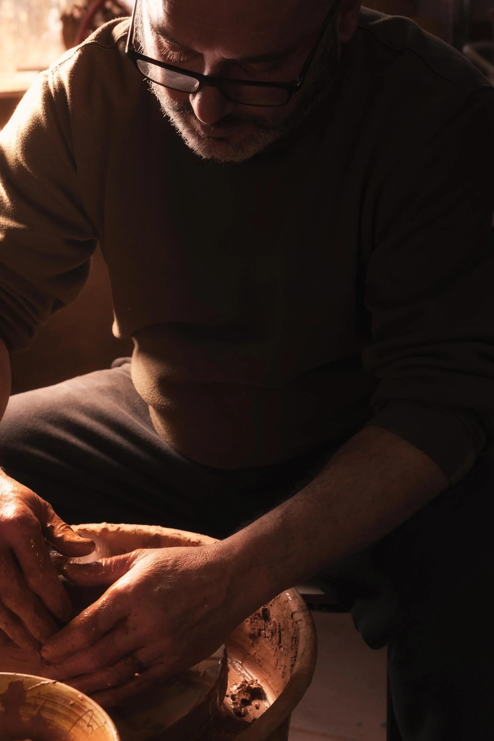 Imagen artística a contraluz de un alfarero trabajando en el torno. Resalta la silueta y el movimiento del barro en el taller de Mondoñedo.