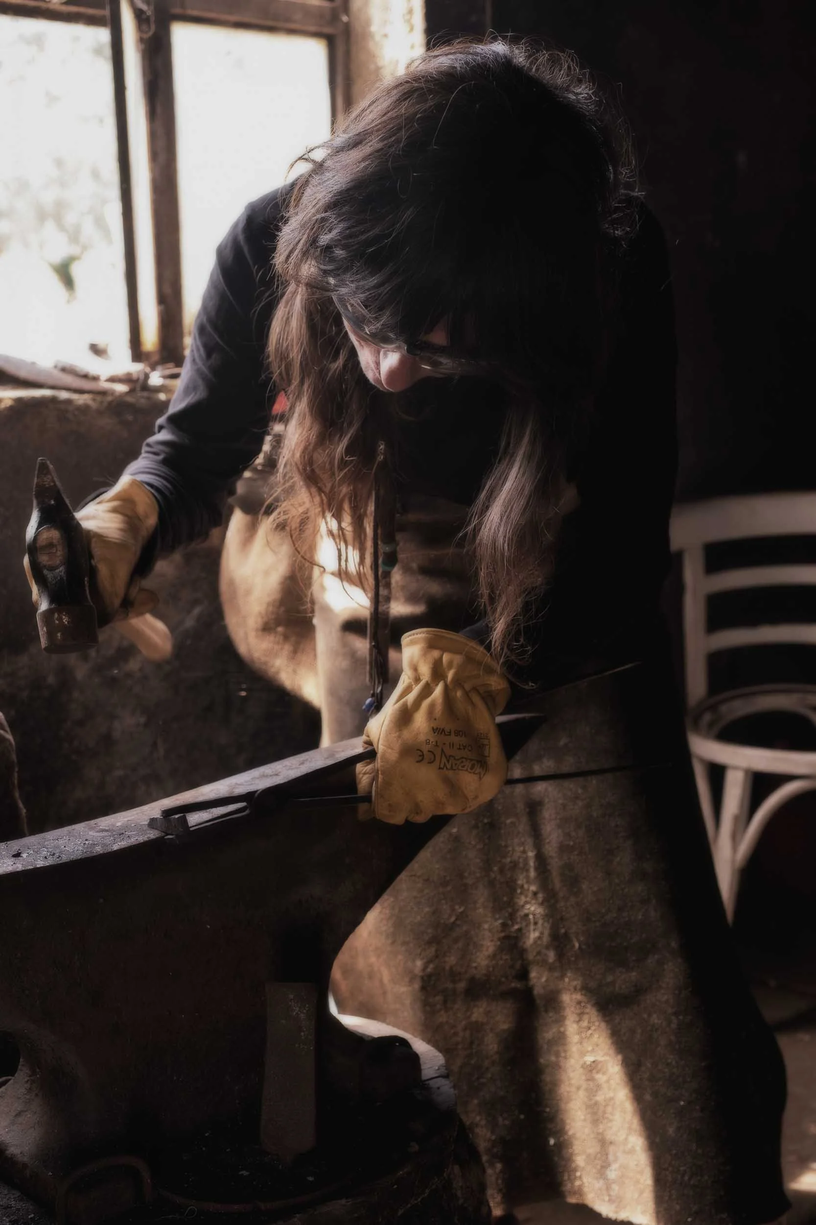 Acción dinámica de martillear una pieza de hierro candente sobre un yunque en la forja de Arenaysal. Captura la energía y la fuerza del oficio.
