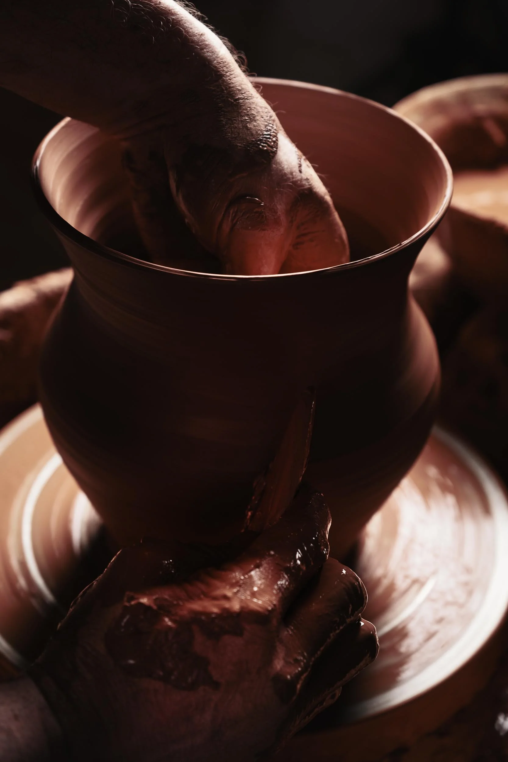 Primer plano de las manos de un artesano moldeando delicadamente el barro húmedo en el torno. Fotografía que resalta el tacto y la forma.