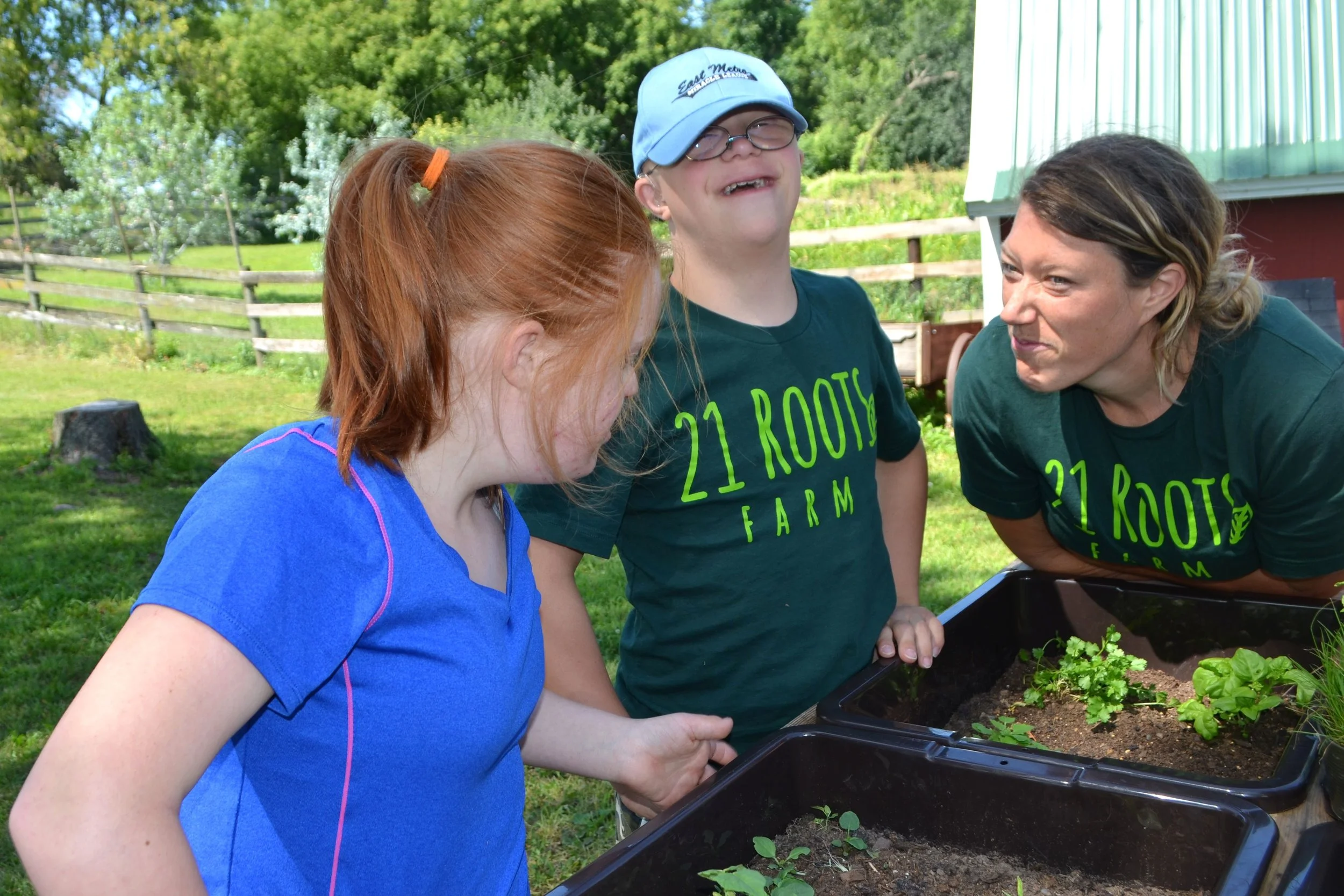 Three people gathered around herbs growing. One woman is looking at the other two making a silly face. 