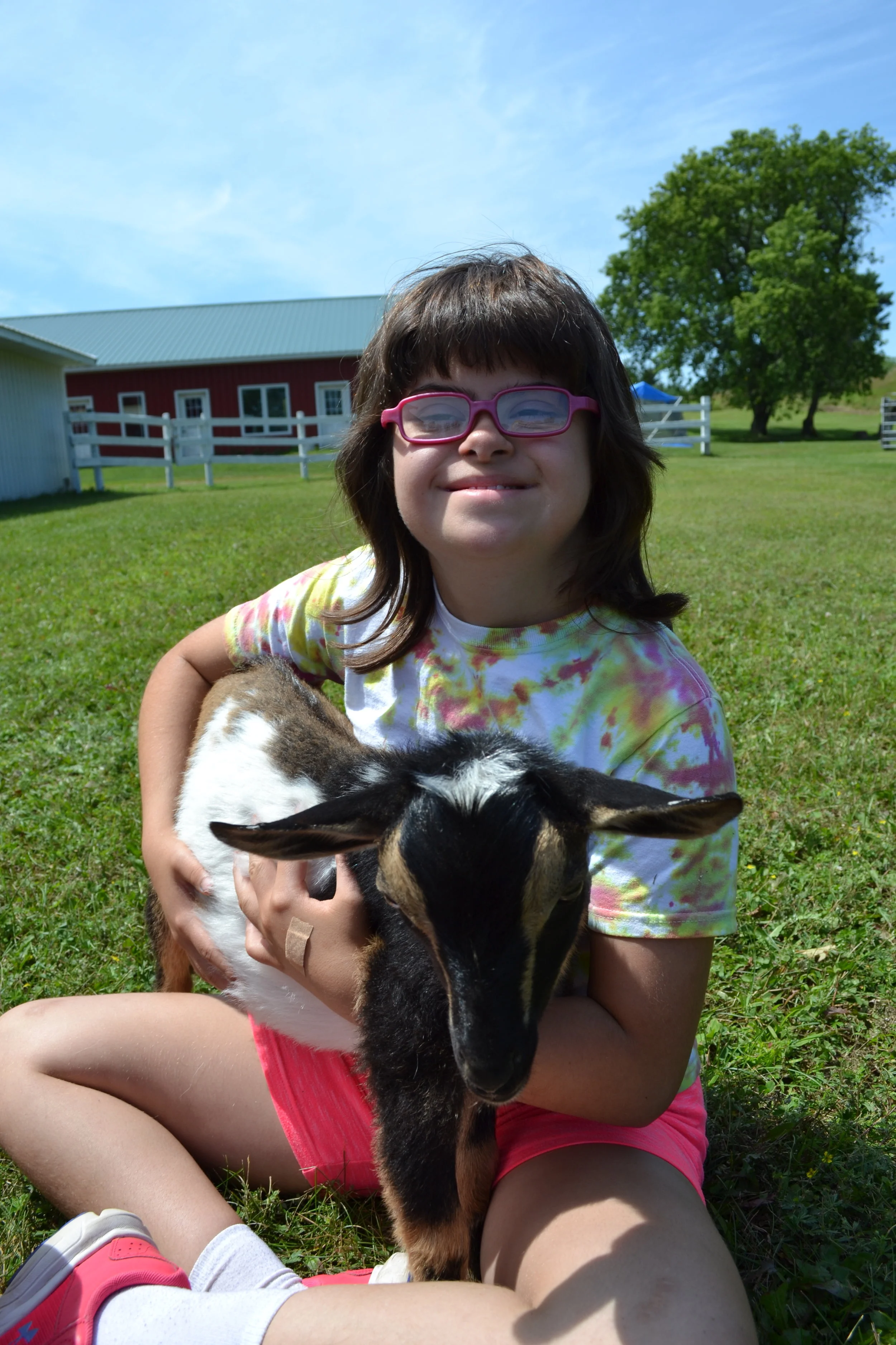 A young lady with glasses smiles at the camera and proudly holds a goat.