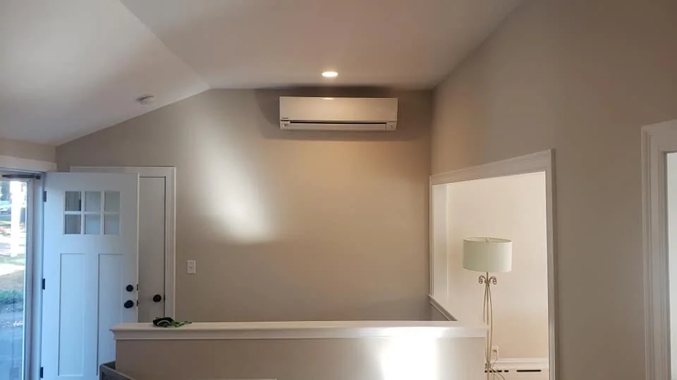 Interior of a room with a white door, a wall-mounted air conditioning unit, a floor lamp, and a partial view of a window with blinds.