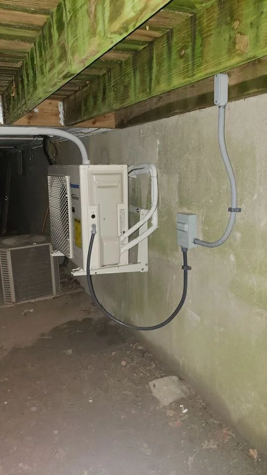 Electrical wiring and an outdoor HVAC unit installed on a concrete wall in a basement or crawl space