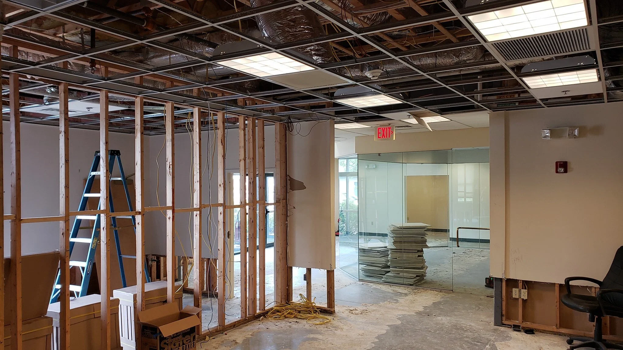 Interior of a commercial space under renovation, with exposed ceiling framework, construction materials, and a ladder.