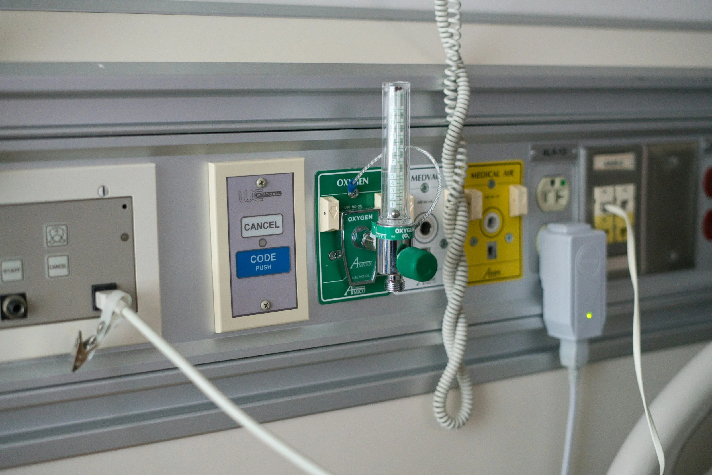 Hospital bed control panel with oxygen regulator, pulse oximeter, and electrical outlets.
