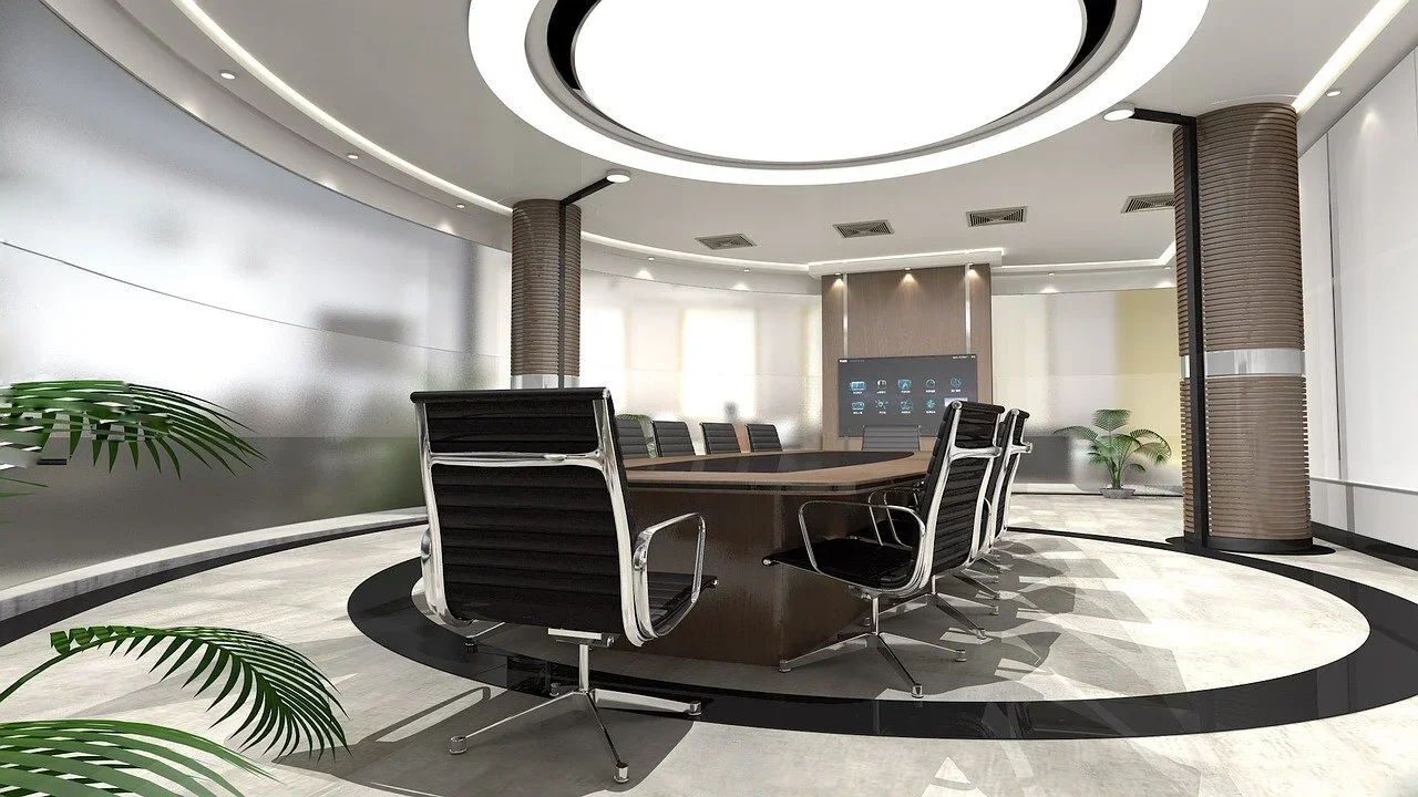 Empty modern conference room with a large oval table and black office chairs, potted plants, and a large digital display on the wall.