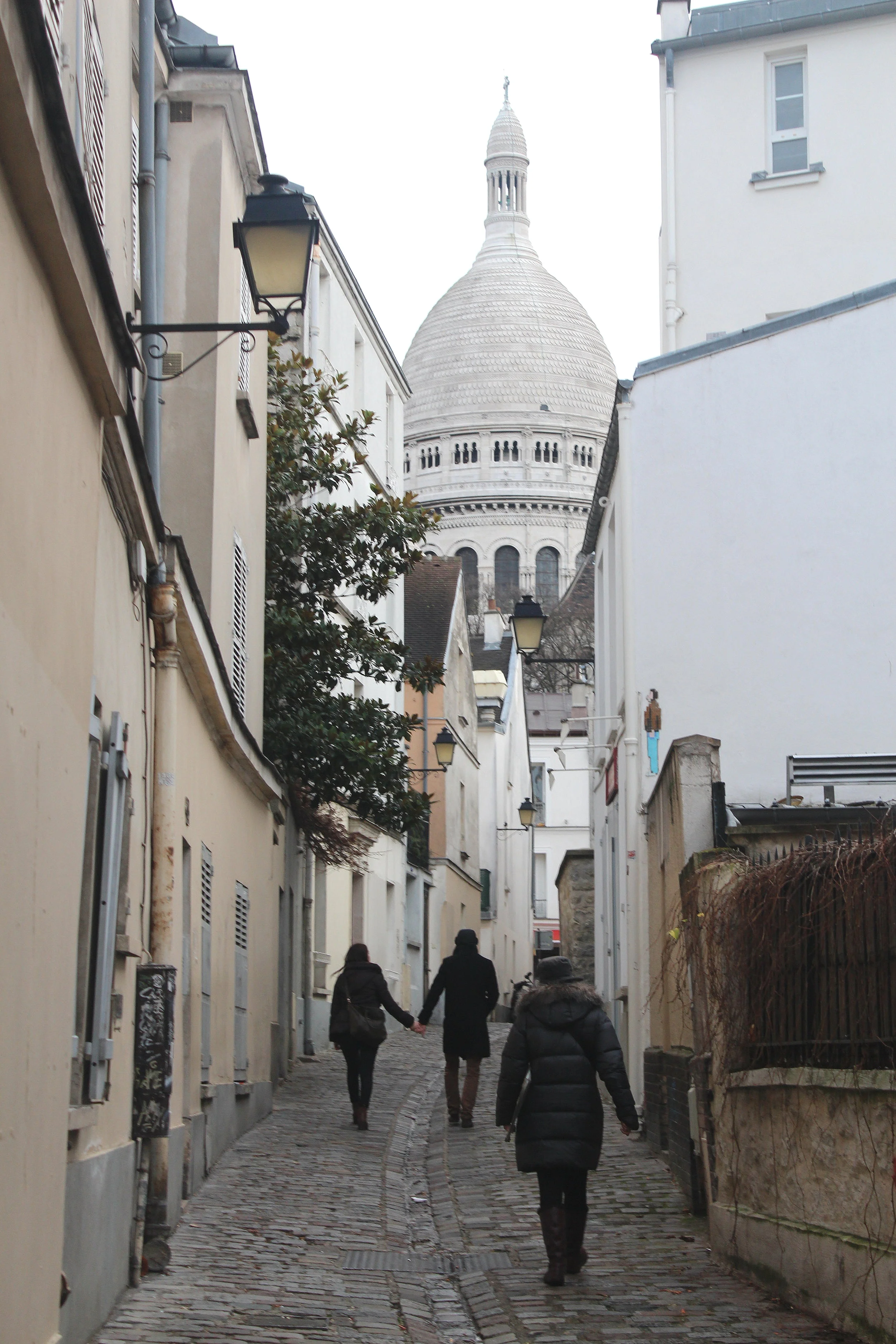 Sacré-Cœur Basilica rising above a narrow cobblestone street in Montmartre, Paris.