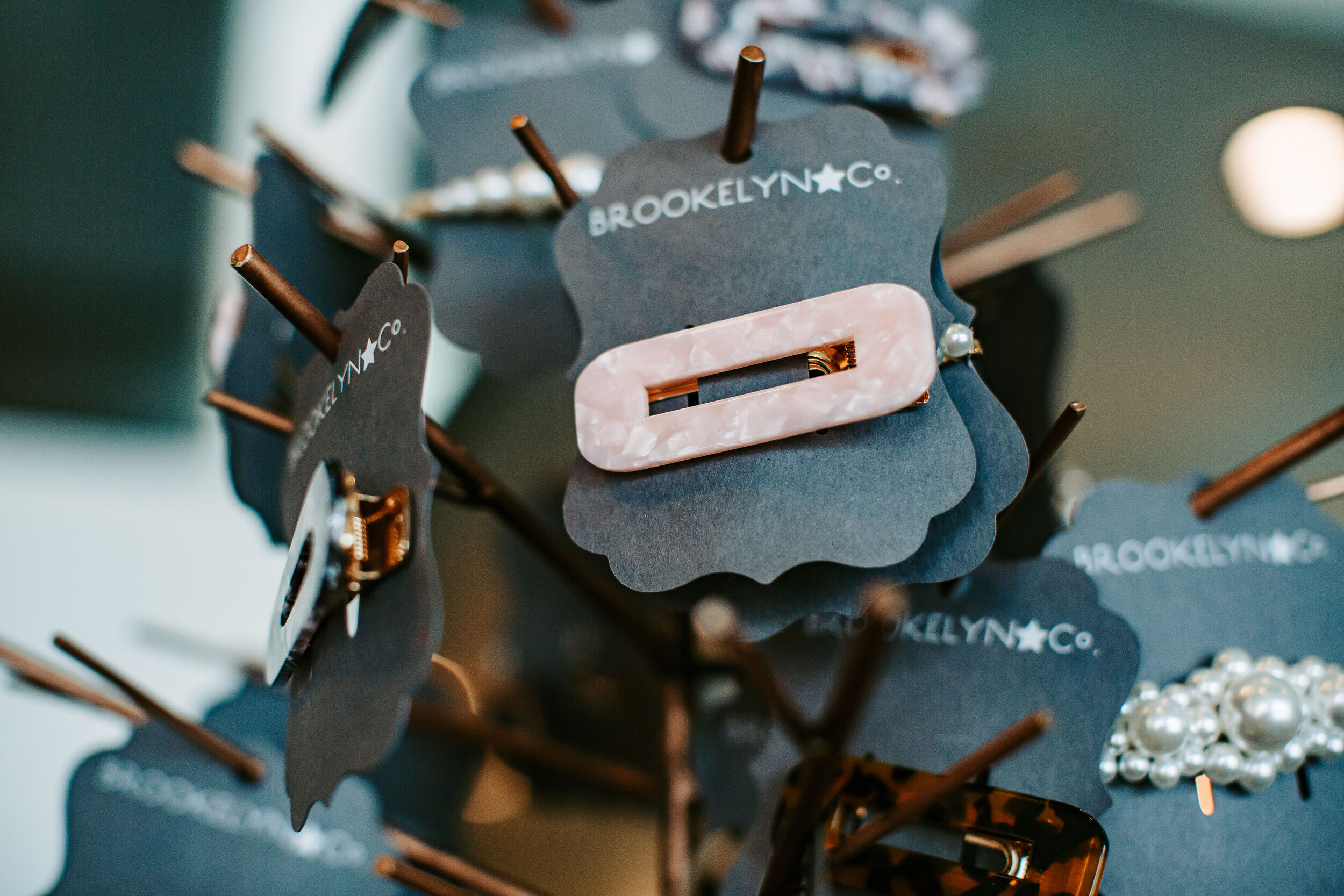  A pink modern hair barrette is hanging on display along with other similar hair clips. The packaging reads Brookelyn &amp; Co. 
