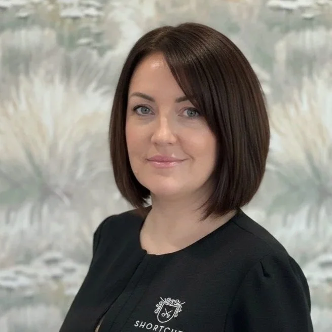 Nainen katsoo kameraan, takana pehmeät valkoisen ja vihreän sävyiset kasvit. Parturi-kampaaja Elena, Shortcut TELAKKARANTA